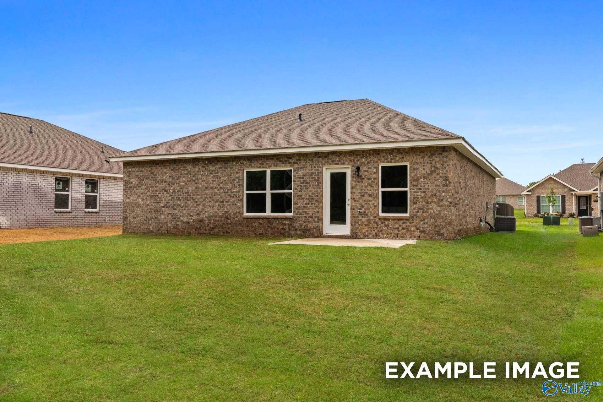Rear view of brick single-story home with covered patio, large windows, lush green yard in Wood Trail, Toney, Alabama