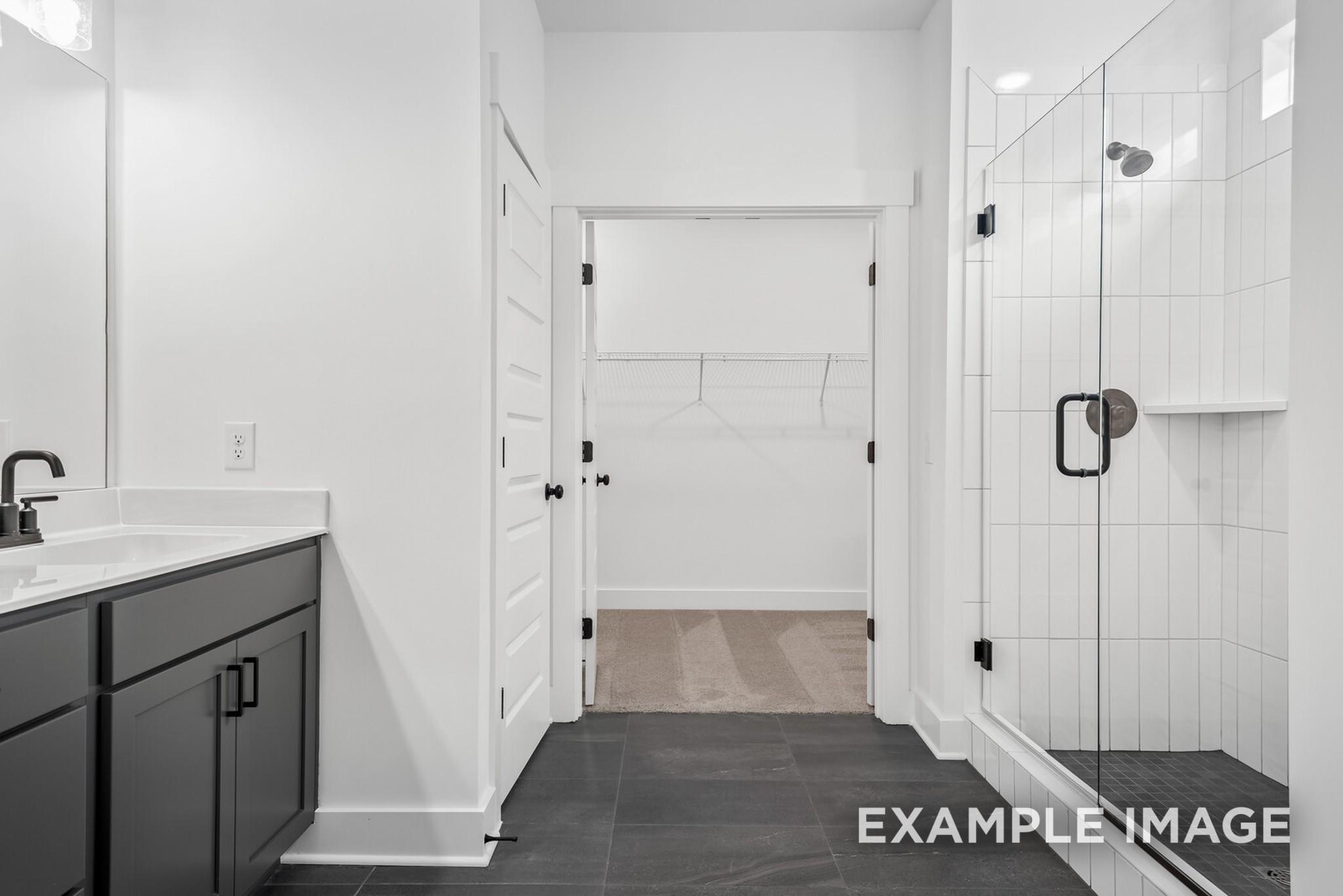Modern master bathroom with dark vanity, frameless glass shower, and walk-in closet in Davidson Homes Ridgeport C, Gallatin, TN