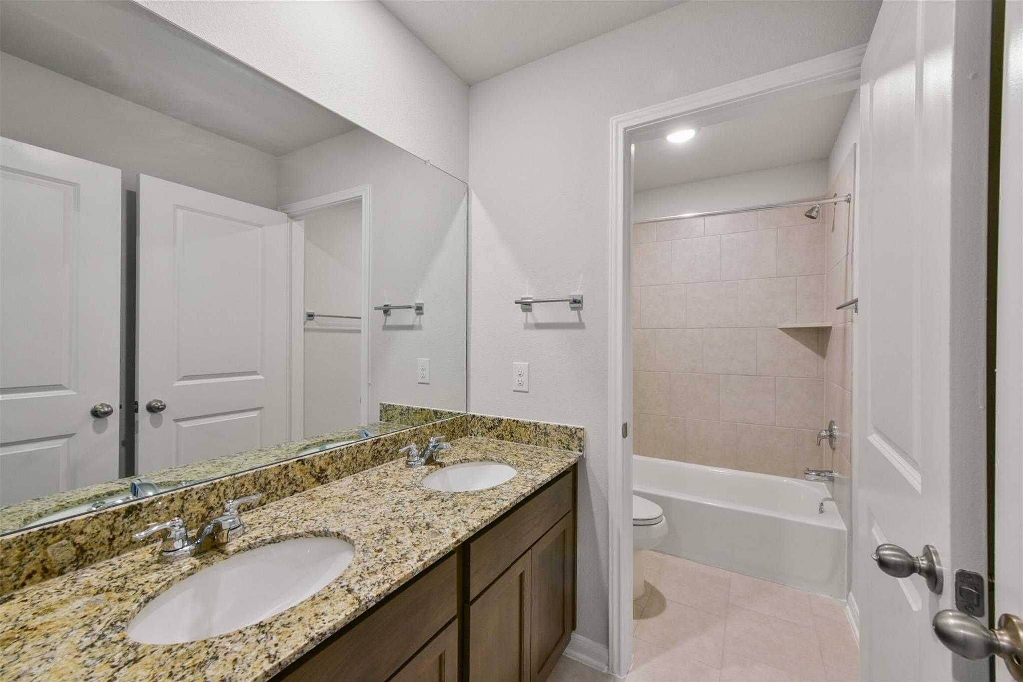 Elegant double vanity with granite counters, soaking tub, and tiled shower in Davidson Homes The Sabine E bathroom, Dayton, Texas