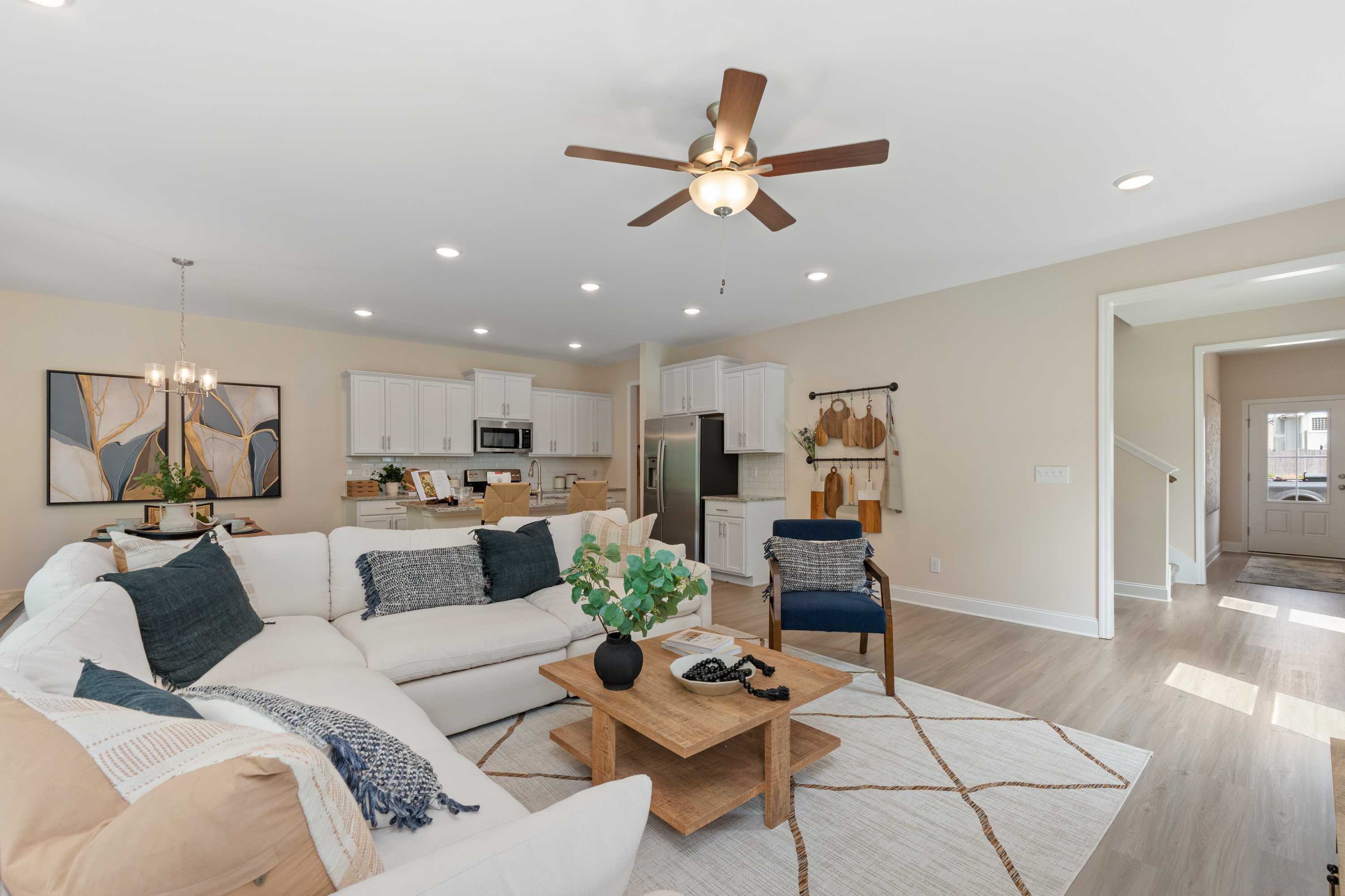 Open-concept living room at Pavilion in Huntsville AL with white L-shaped sofa, ceiling fan, hardwood floors, and kitchen view