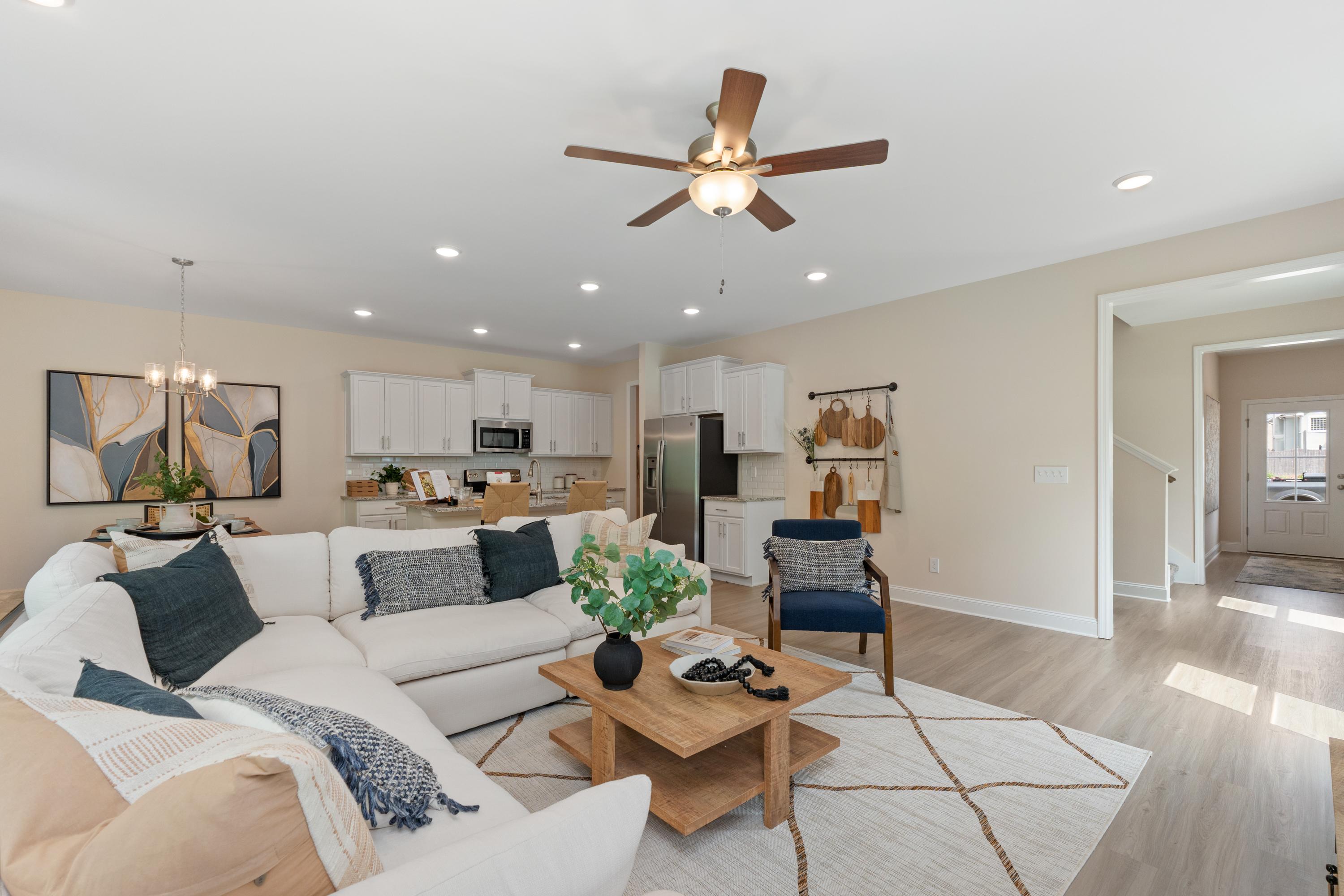 Open-concept living room at Pavilion in Huntsville AL with white L-shaped sofa, ceiling fan, hardwood floors, and kitchen view