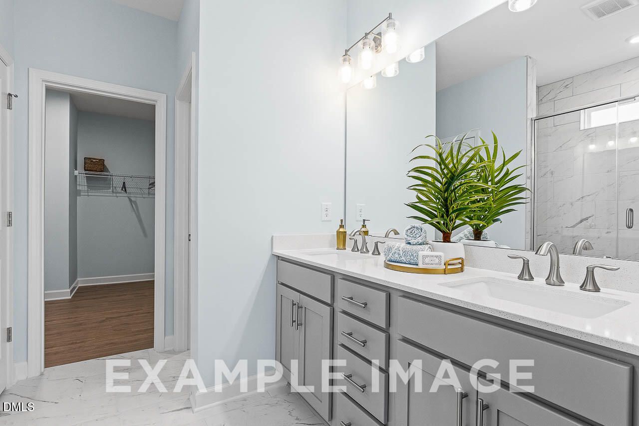 Dual vanity bathroom with gray cabinets, quartz countertops, and walk-in shower in The Ash C floor plan, Lillington, NC