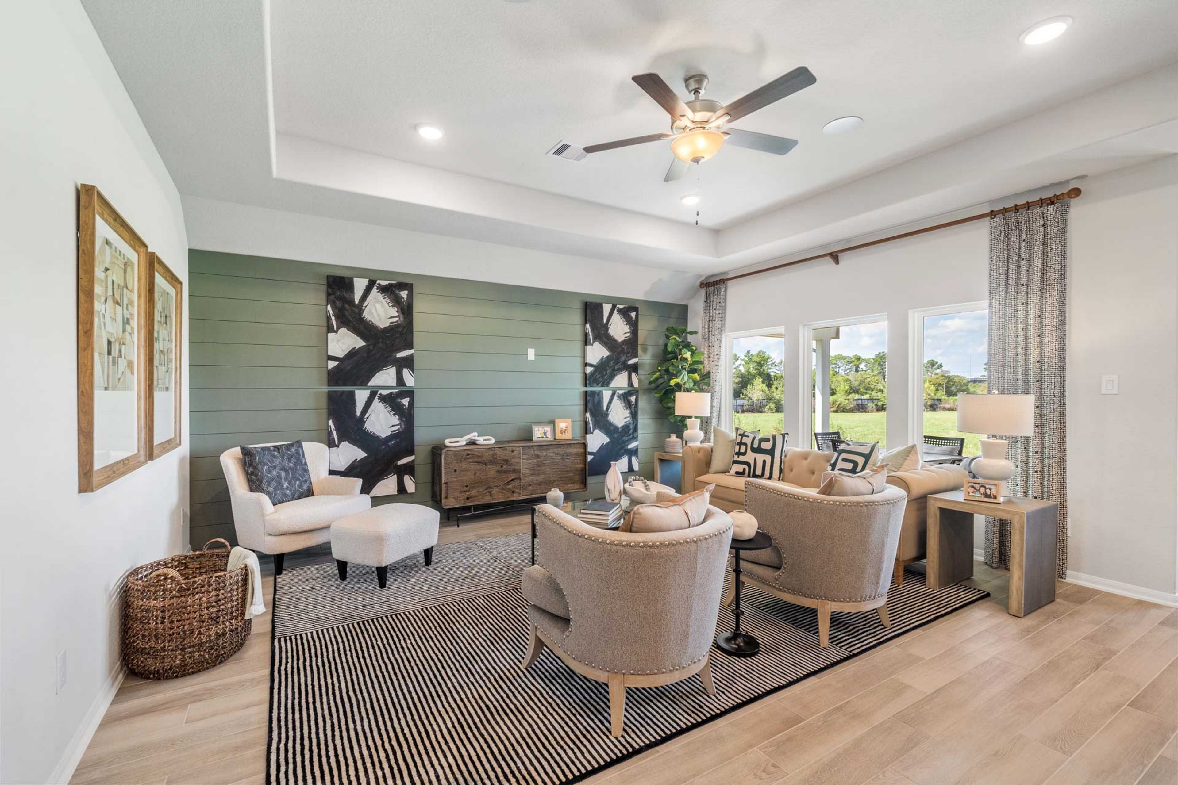 Spacious living room at Windmill Estates in Magnolia Texas with green accent wall, abstract art, ceiling fans, white armchairs, hardwood floors, and large windows