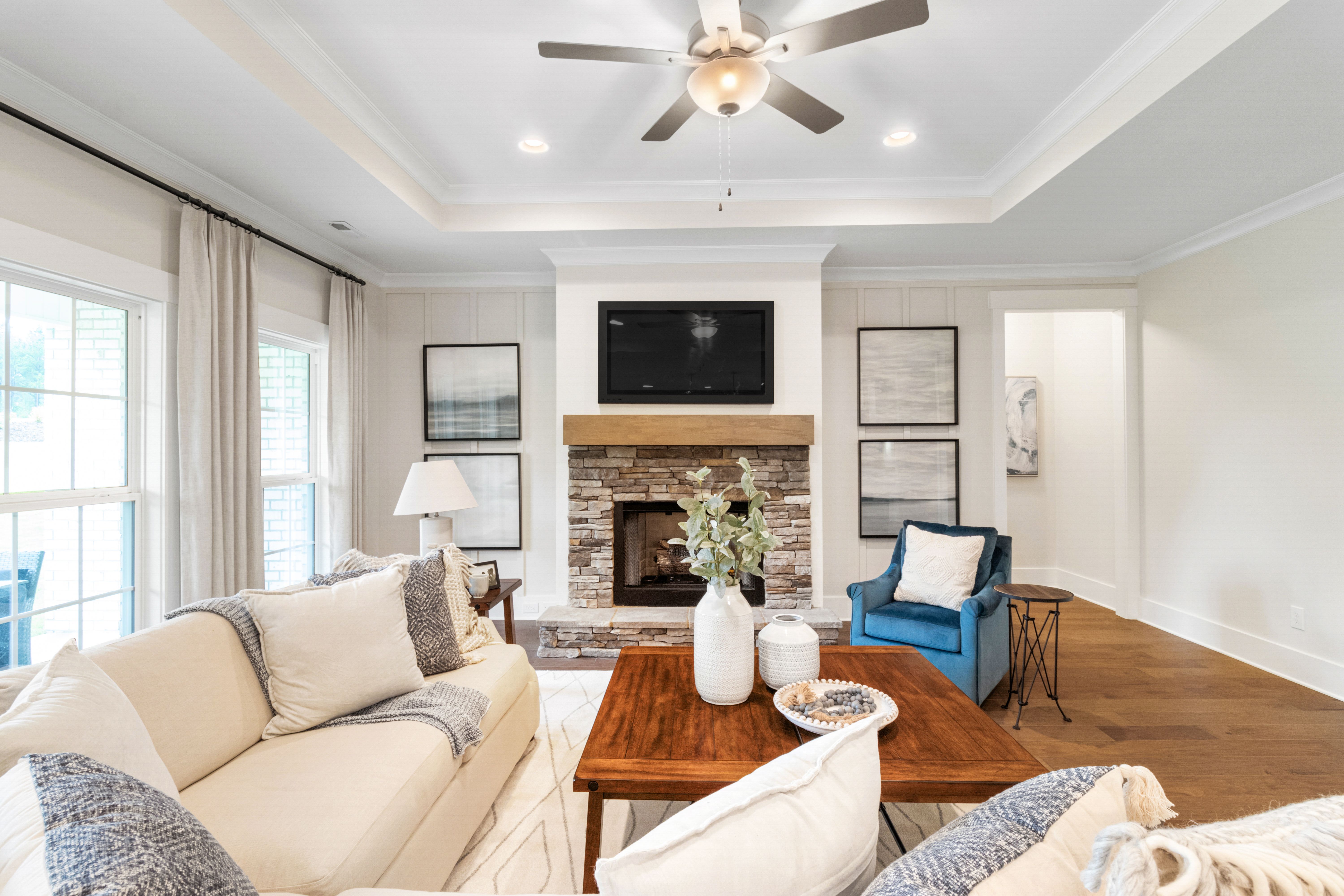 Cozy living room at Noble Ridge in Cullman Alabama with stone fireplace, beige sofa, wooden coffee table, ceiling fan, and hardwood floors