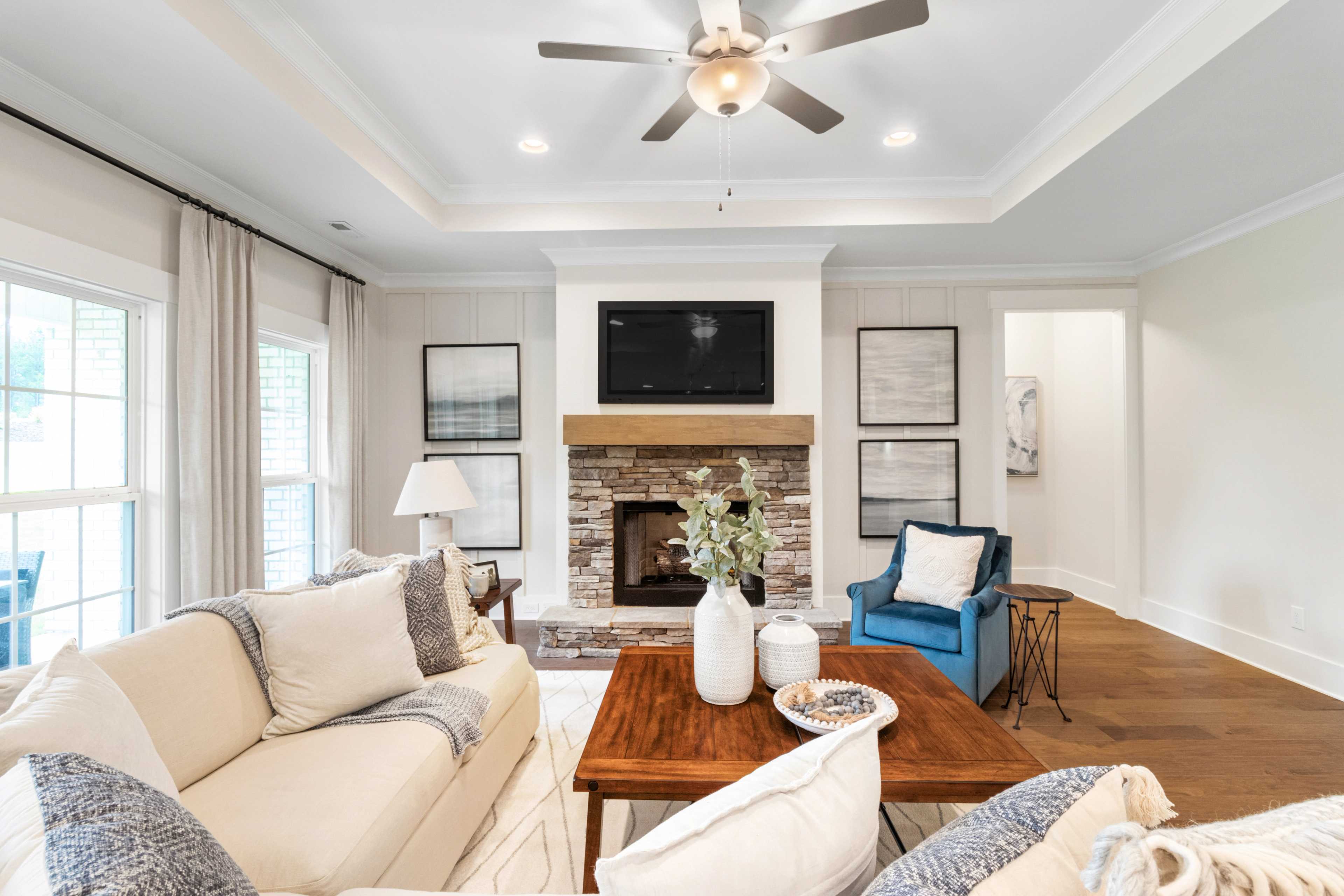 Cozy living room at Noble Ridge in Cullman Alabama with stone fireplace, beige sofa, wooden coffee table, ceiling fan, and hardwood floors