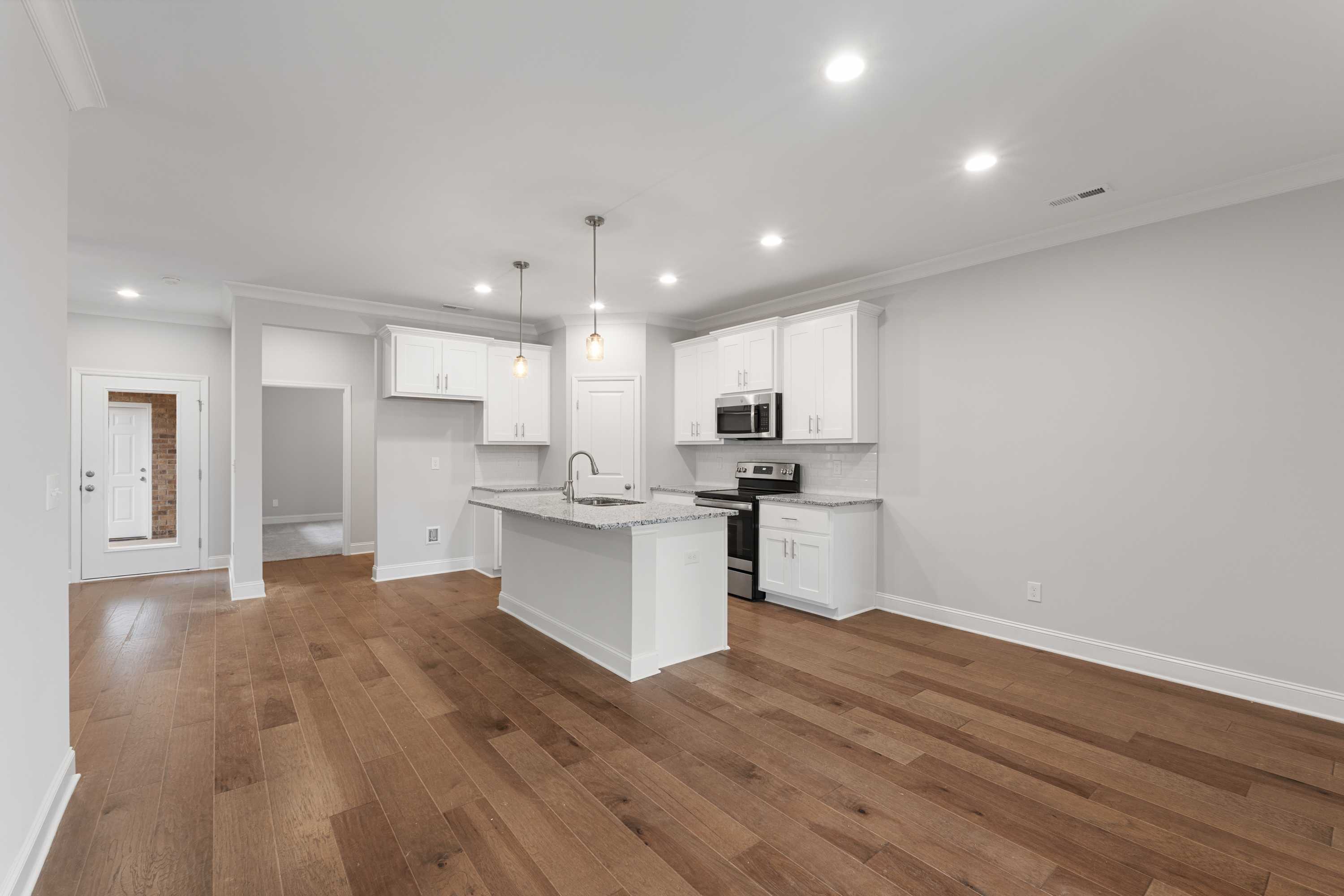 Modern kitchen in The Copeland B showcasing white cabinets, large center island, stainless steel appliances, and hardwood floors
