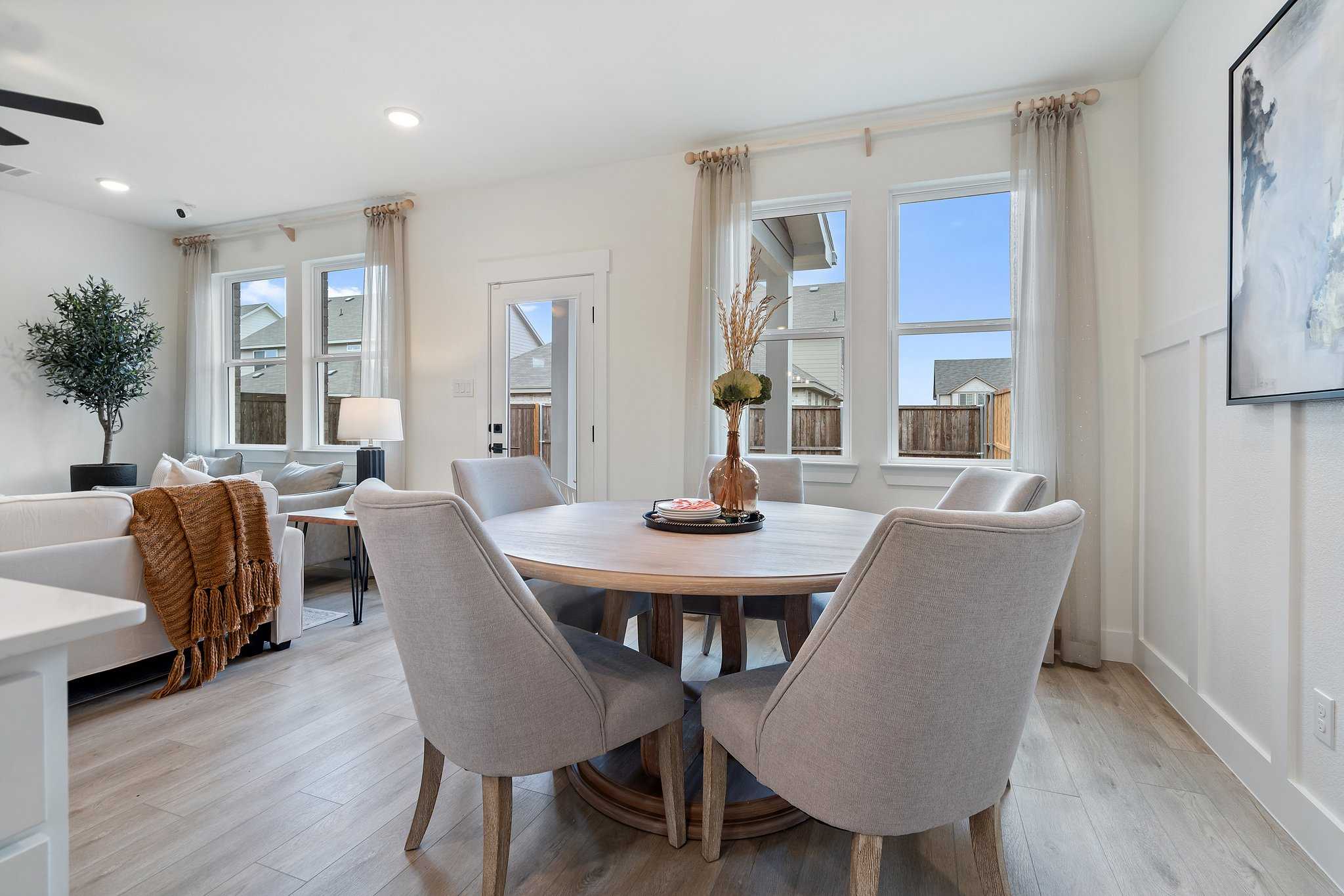 The Wake dining room featuring round wooden table, gray upholstered chairs, potted olive tree, and open living space