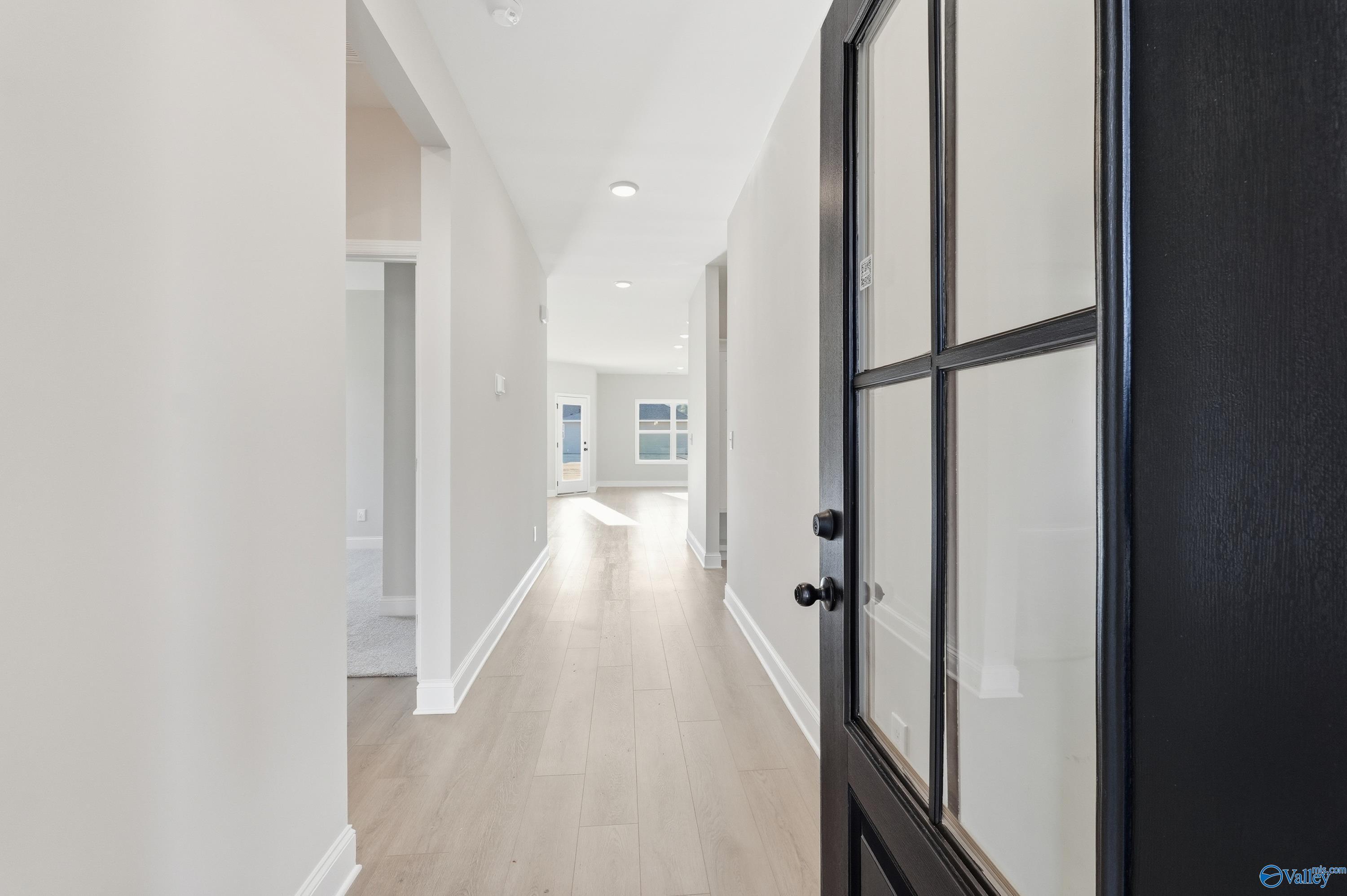 Bright hallway with light oak floors, white walls, and black glass-paneled front door in Davidson Homes The Franklin E, Hazel Green, AL