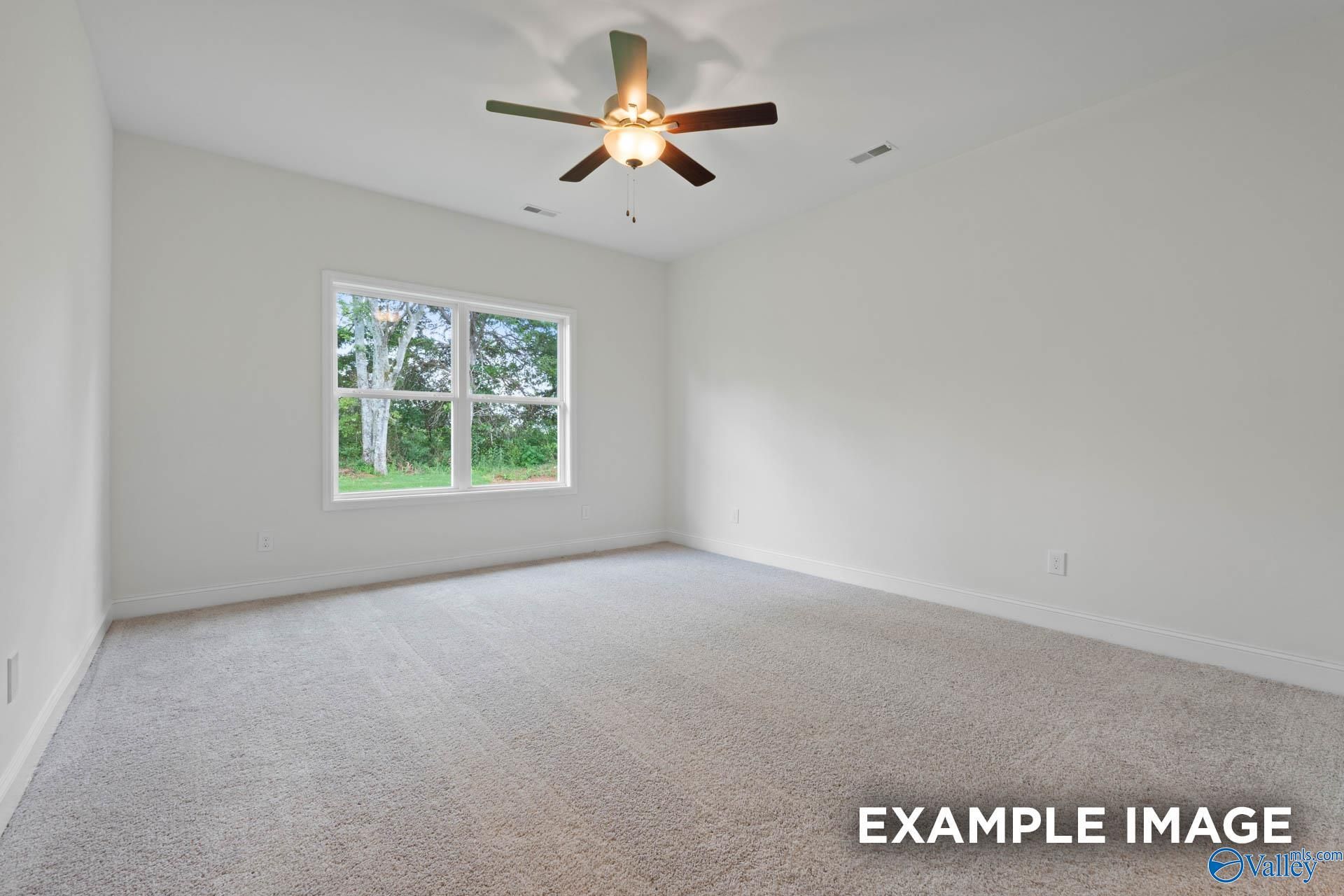Empty secondary bedroom with ceiling fan, large window overlooking trees, and carpeted floors in Evermore Homes The Daphne E, Harvest, AL