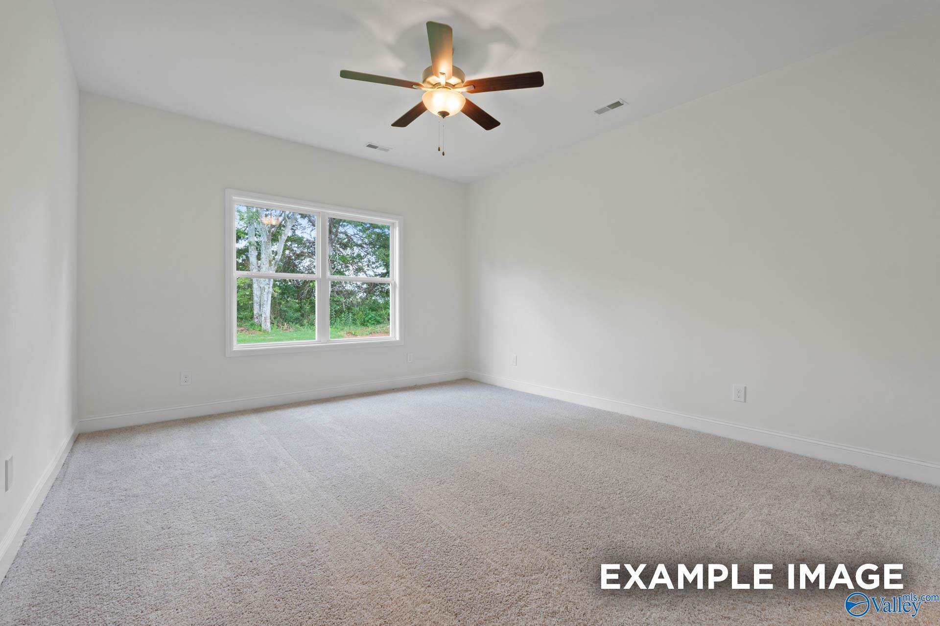 Empty secondary bedroom with ceiling fan, large window overlooking trees, and carpeted floors in Evermore Homes The Daphne E, Harvest, AL