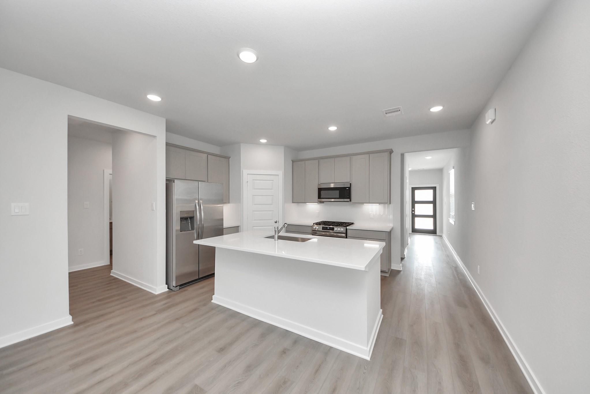 Bright open-concept kitchen with white island, gray shaker cabinets, and stainless appliances in Davidson Homes San Marcos E, Beasley, TX