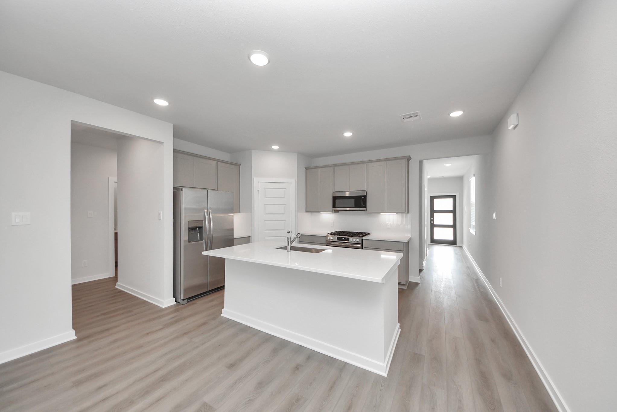 Bright open-concept kitchen with white island, gray shaker cabinets, and stainless appliances in Davidson Homes San Marcos E, Beasley, TX