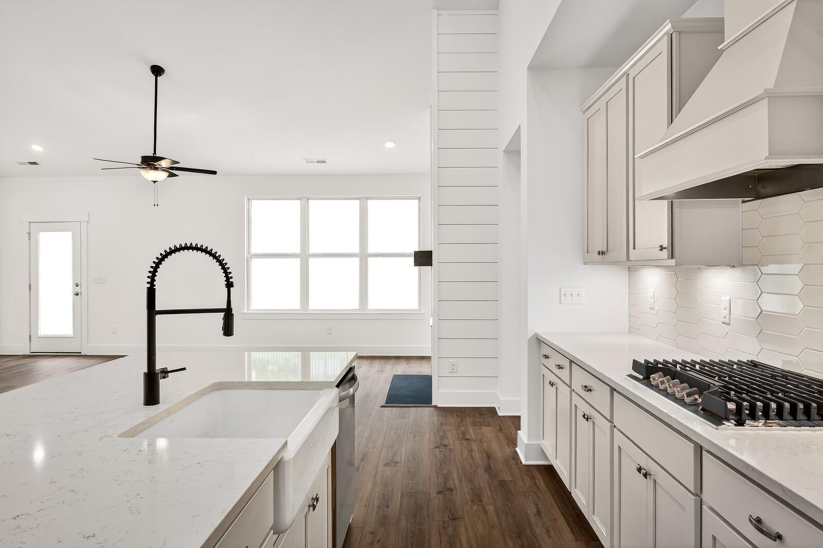 Modern open-concept kitchen with white shaker cabinets, quartz counters, farmhouse sink, and gas range in Davidson Homes Ridgeport C, Gallatin, TN