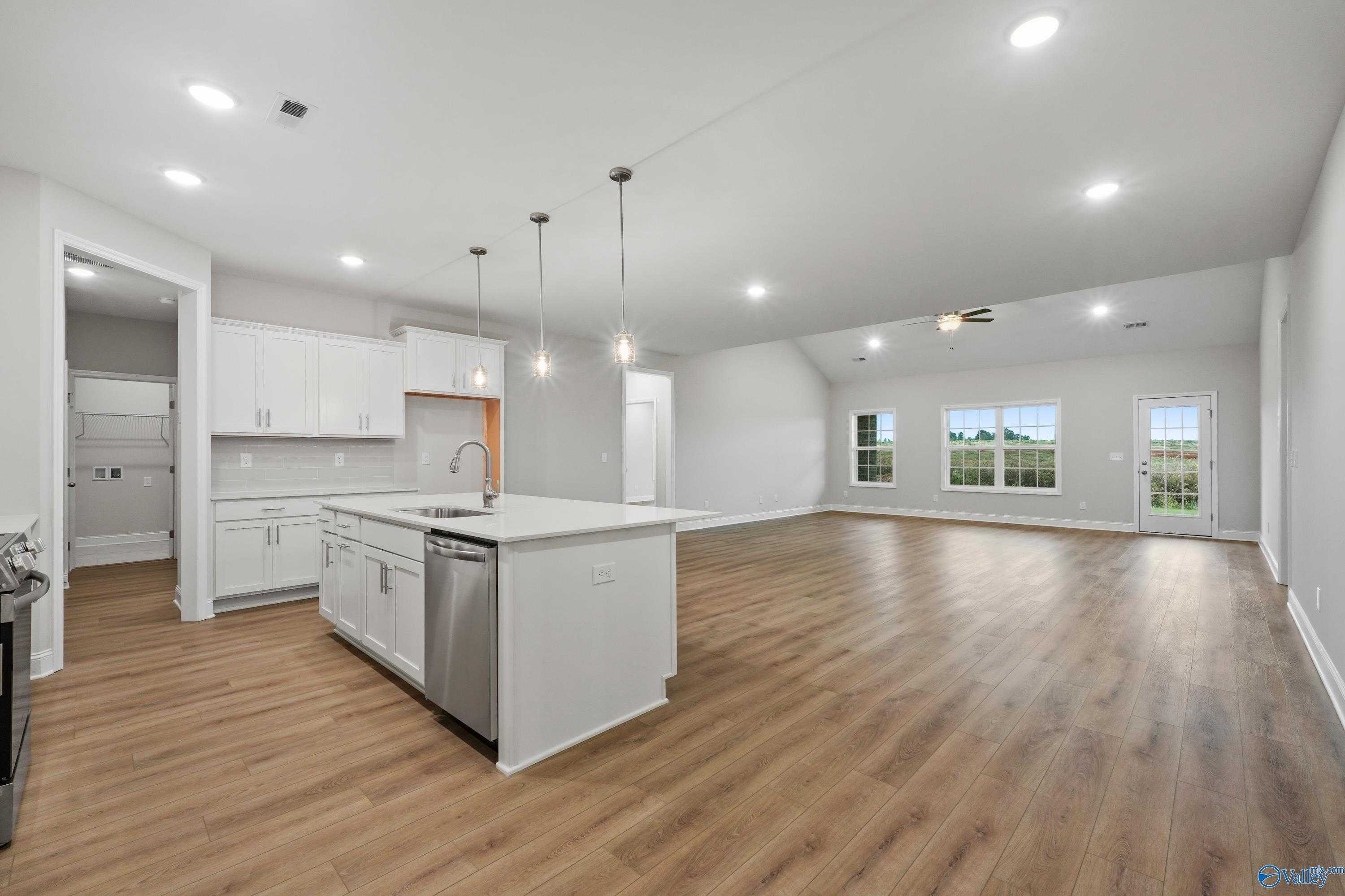 Open-concept kitchen with white island, sink, dishwasher, hardwood floors, and large windows in Davidson Homes The Lanier, Harvest AL