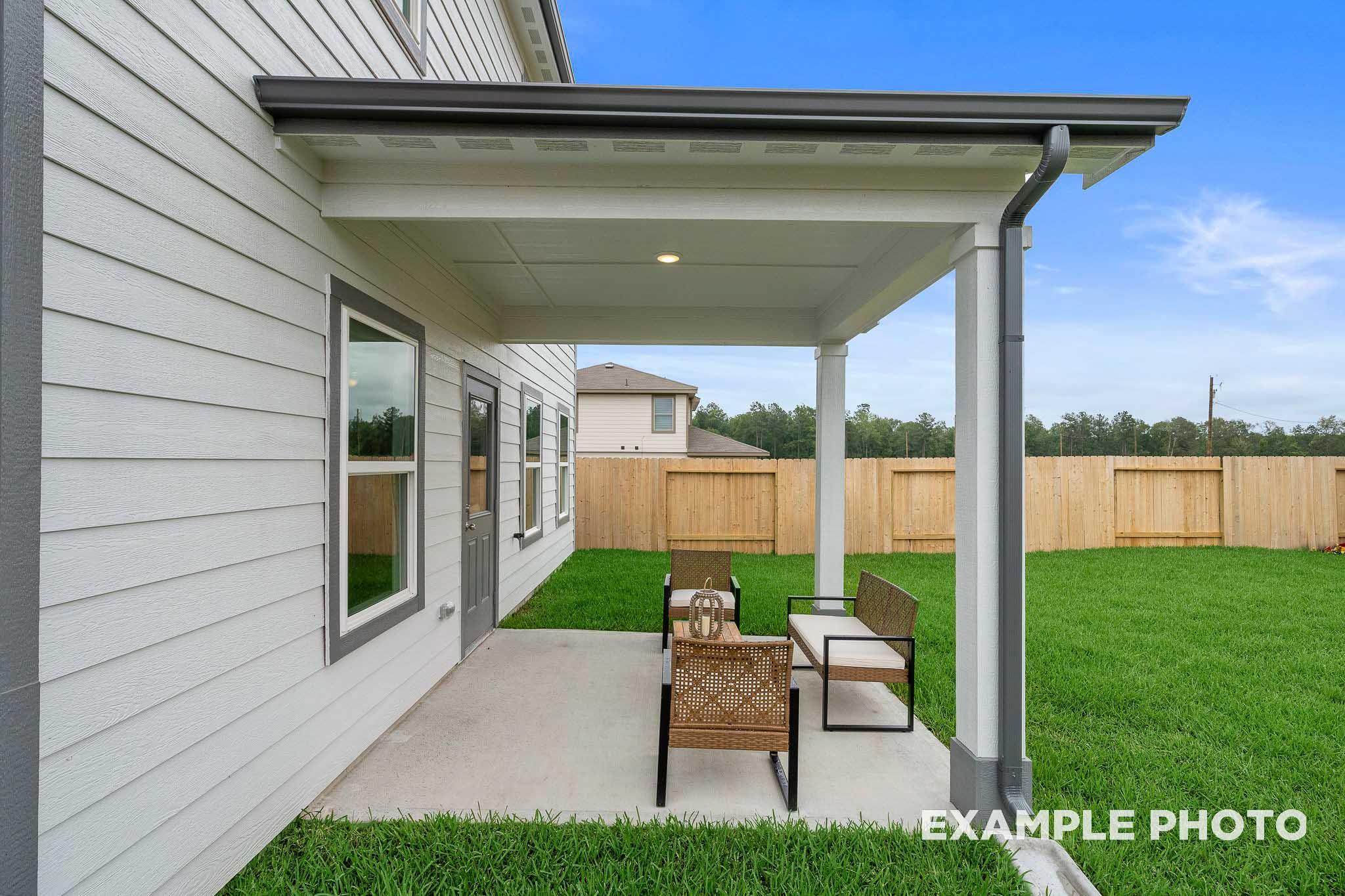 Covered patio of The Trinity home by Davidson Homes featuring wicker furniture, lush green lawn, and wooden fence in Beasley, Texas
