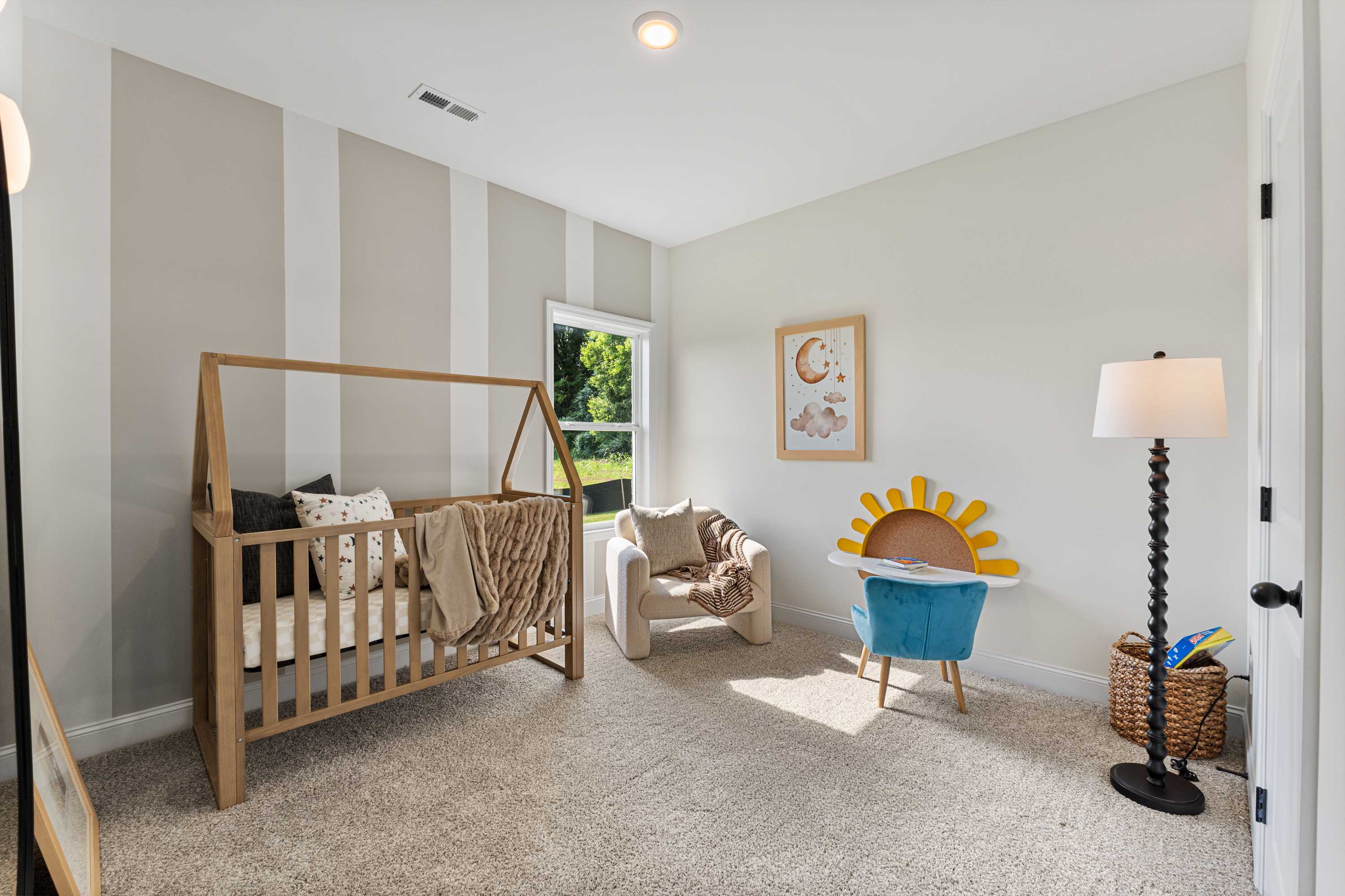 Cozy nursery at Lynn Meadows in Meridianville Alabama featuring wooden A-frame crib, striped beige walls, and whimsical art