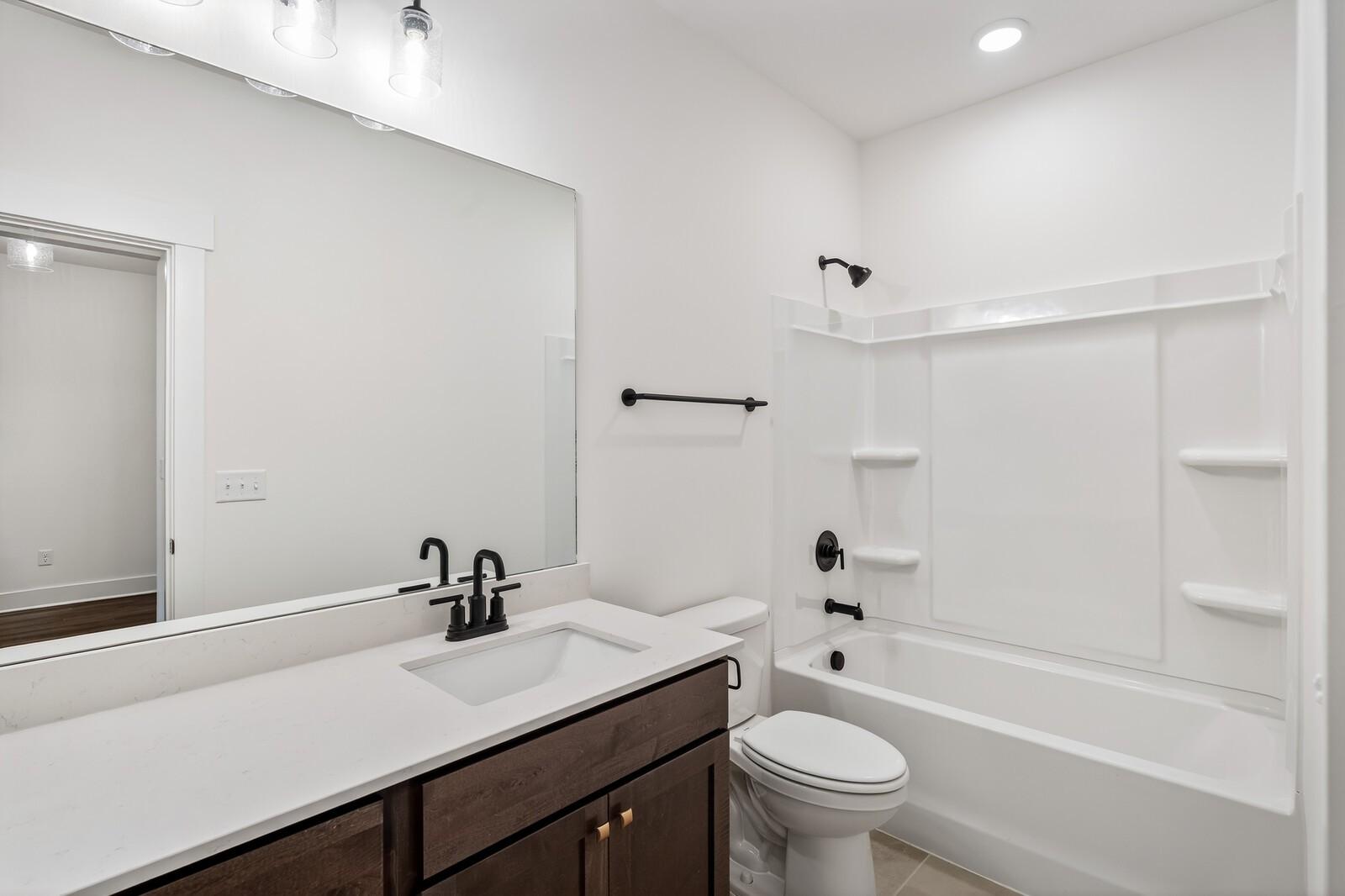 Modern white bathroom with alcove tub, glass shower, quartz vanity, and black fixtures in Davidson Homes Ridgeport C, Gallatin TN