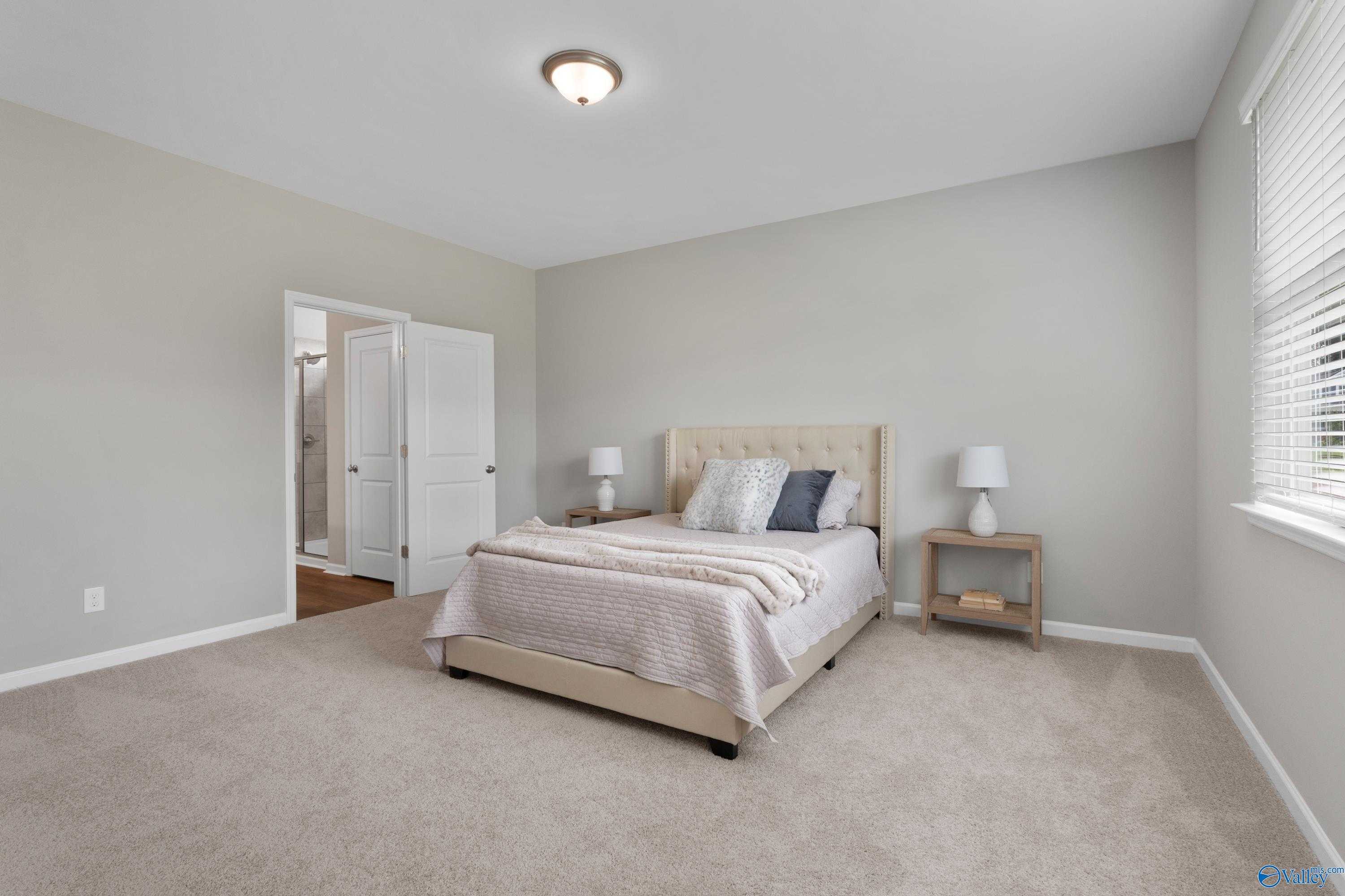 Cozy bedroom with upholstered queen bed, neutral gray walls, carpet flooring, and adjacent bath in Evermore Homes The Noble, Madison, Alabama