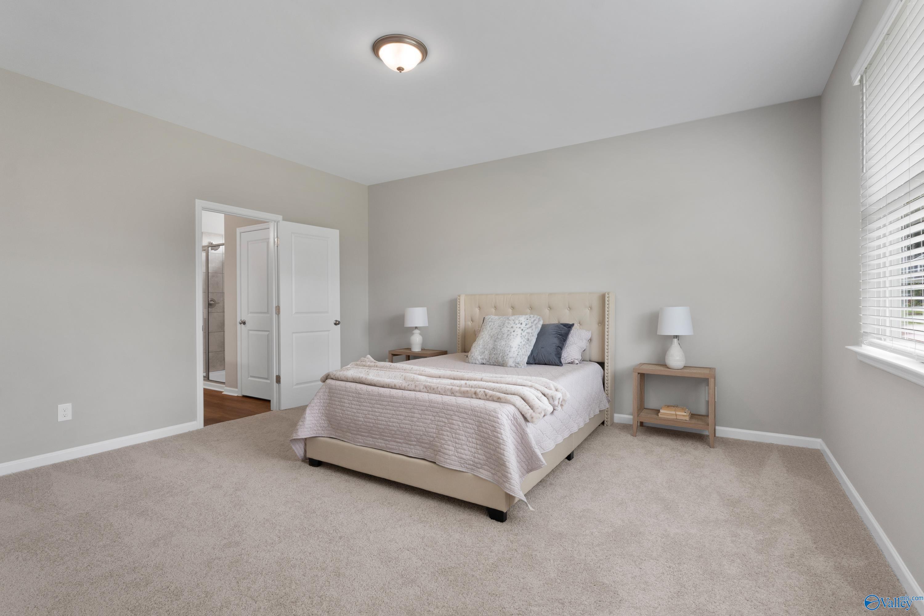 Cozy secondary bedroom with upholstered bed, lamps, en-suite bath in Davidson Homes The Noble, Evergreen Mill, Madison AL