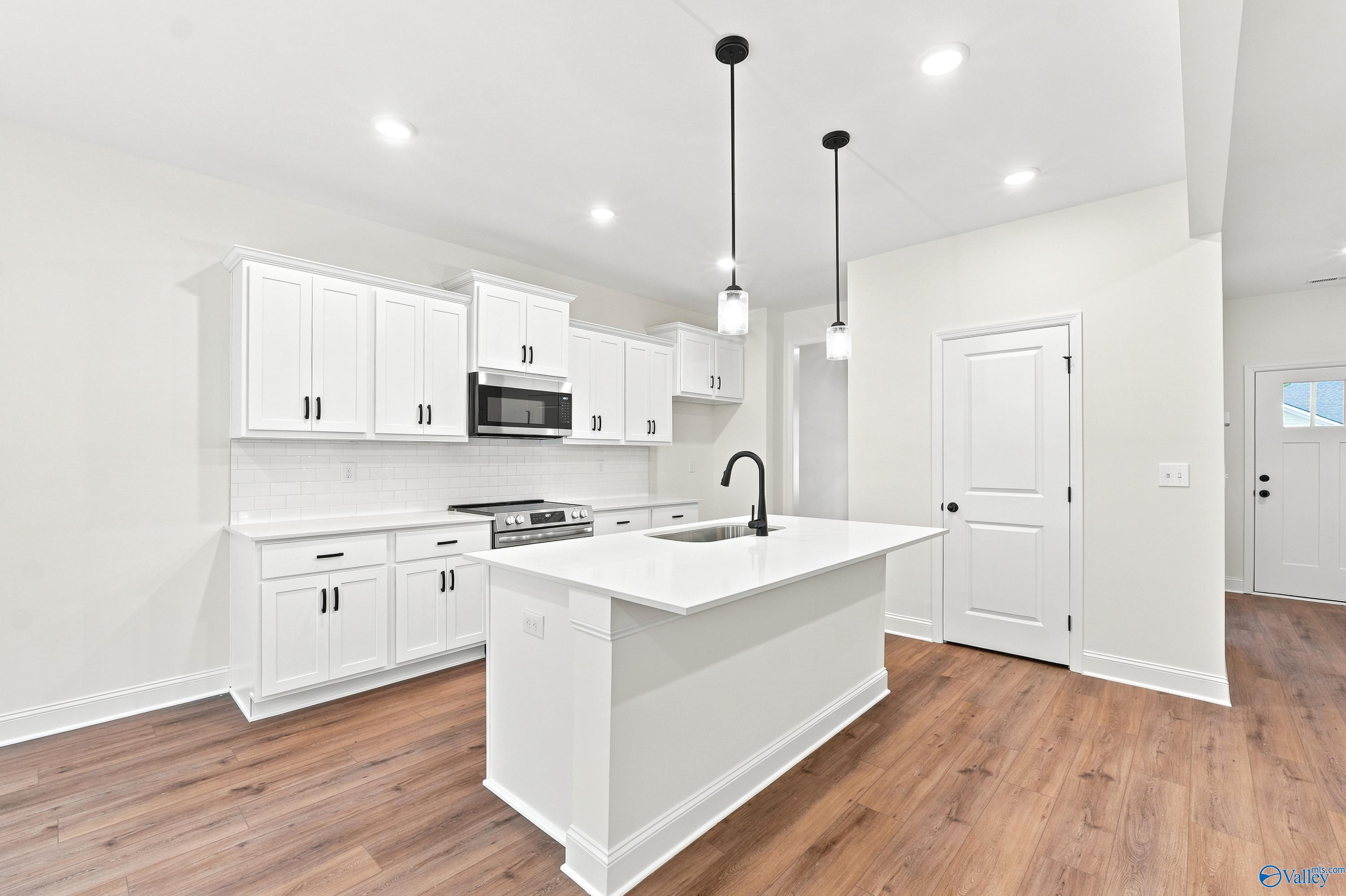 Modern kitchen with white cabinets, center island, and wood floors in The Shelby D floor plan at Noble Ridge, Cullman.