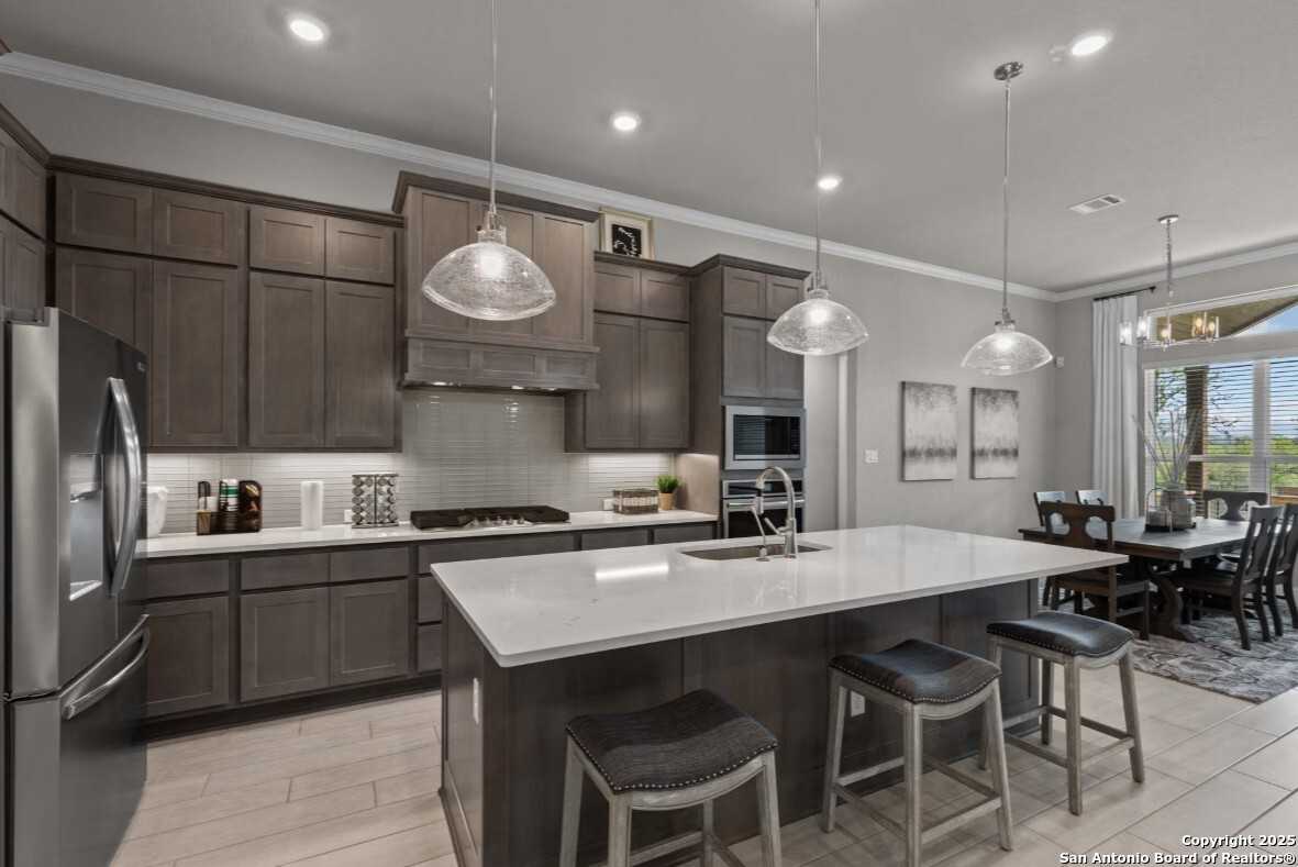 Modern kitchen featuring dark shaker cabinets, quartz island with bar stools, and stainless appliances in Davidson Homes The Garner B, Ladera, San Antonio