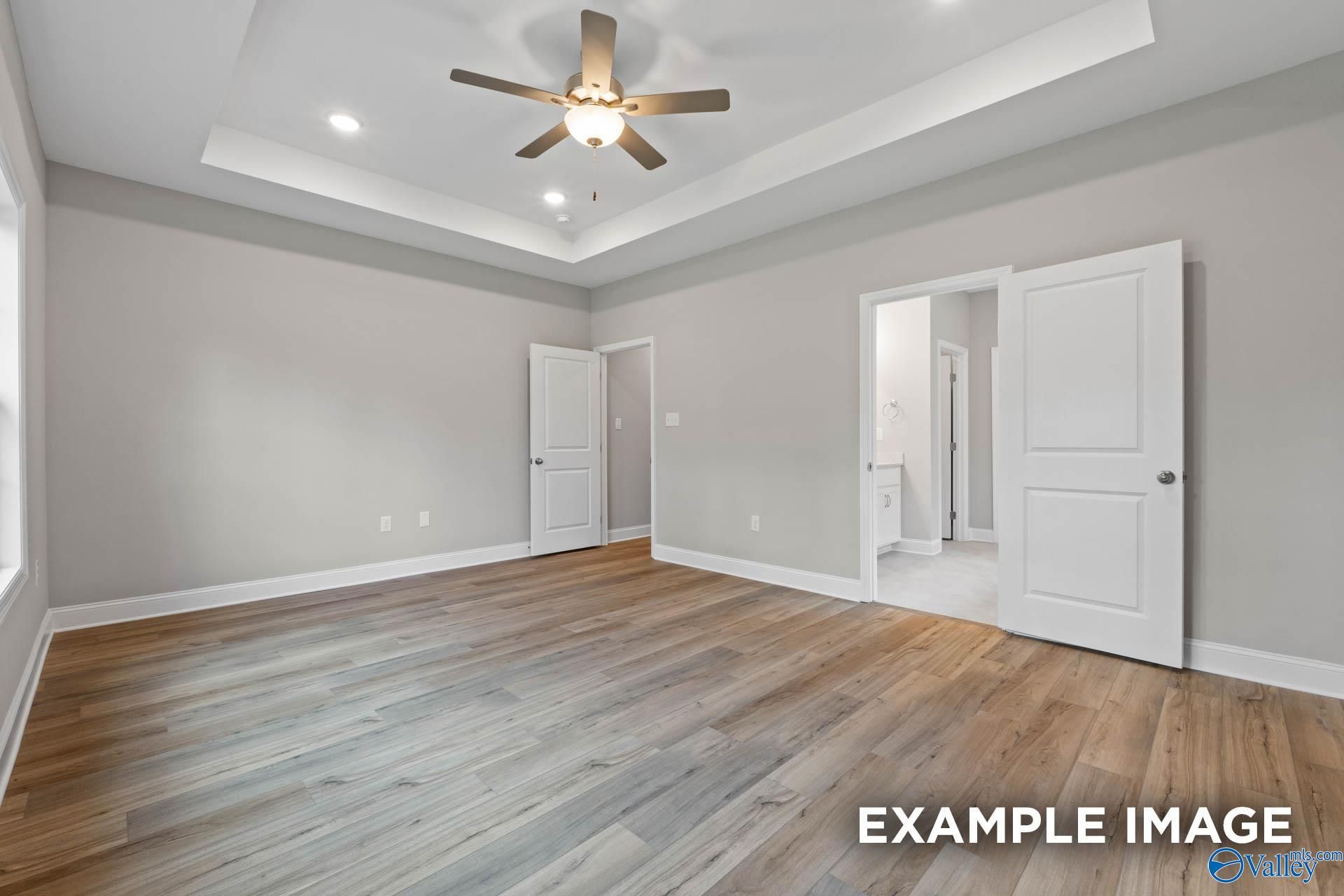 Spacious master bedroom with ceiling fan, open bath door, and light hardwood floors in Davidson Homes The Montgomery, Meridianville AL