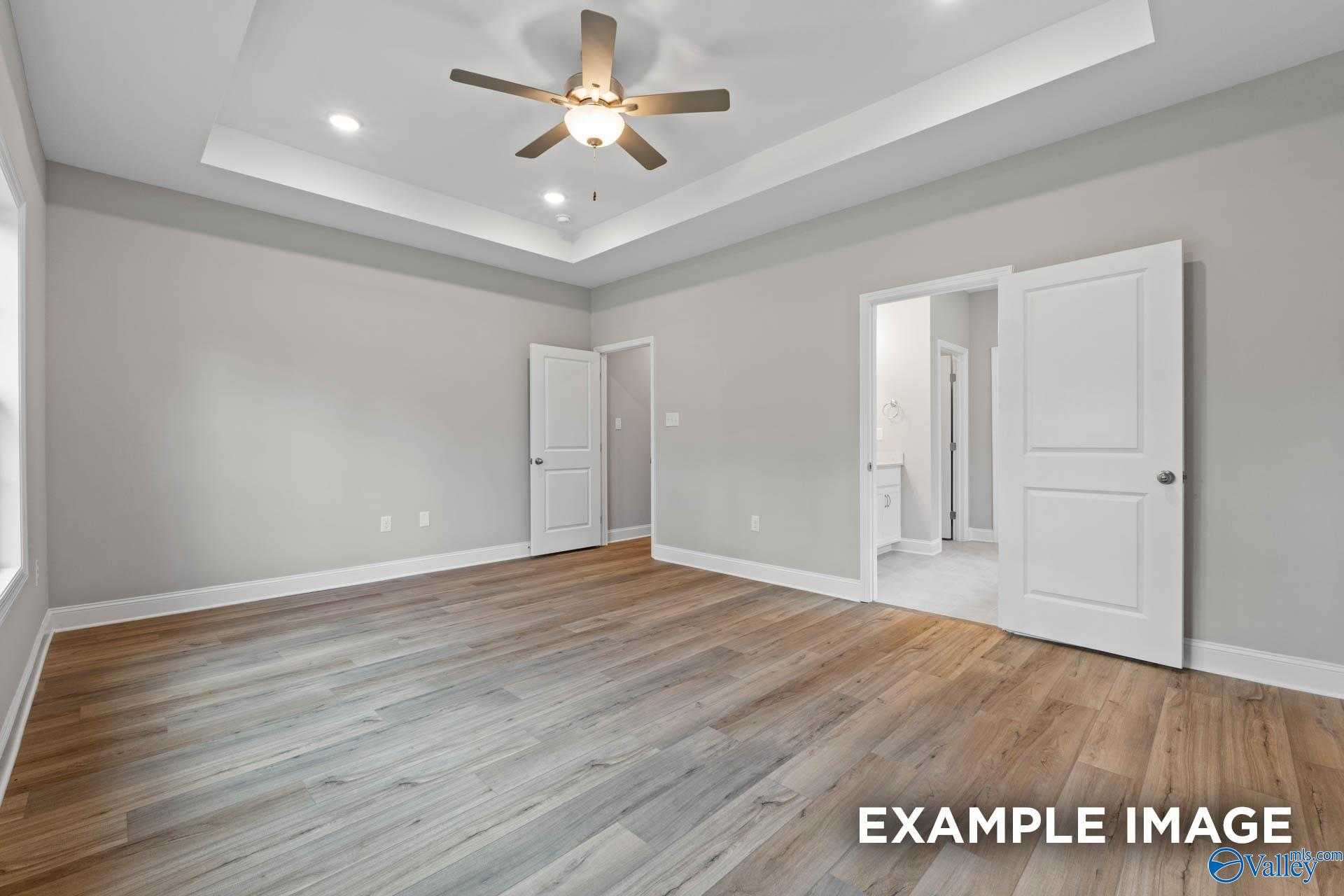 Spacious master bedroom with ceiling fan, open bath door, and light hardwood floors in Davidson Homes The Montgomery, Meridianville AL