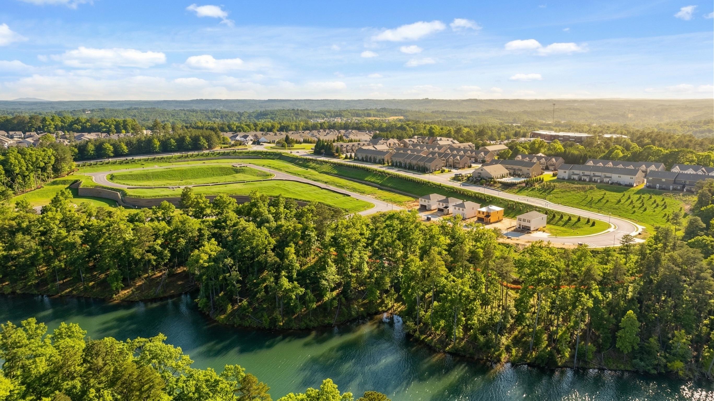 Aerial view of The Bluffs community with rows of new craftsman townhomes, lush green lawns, winding paths, and serene lake in Canton, Georgia
