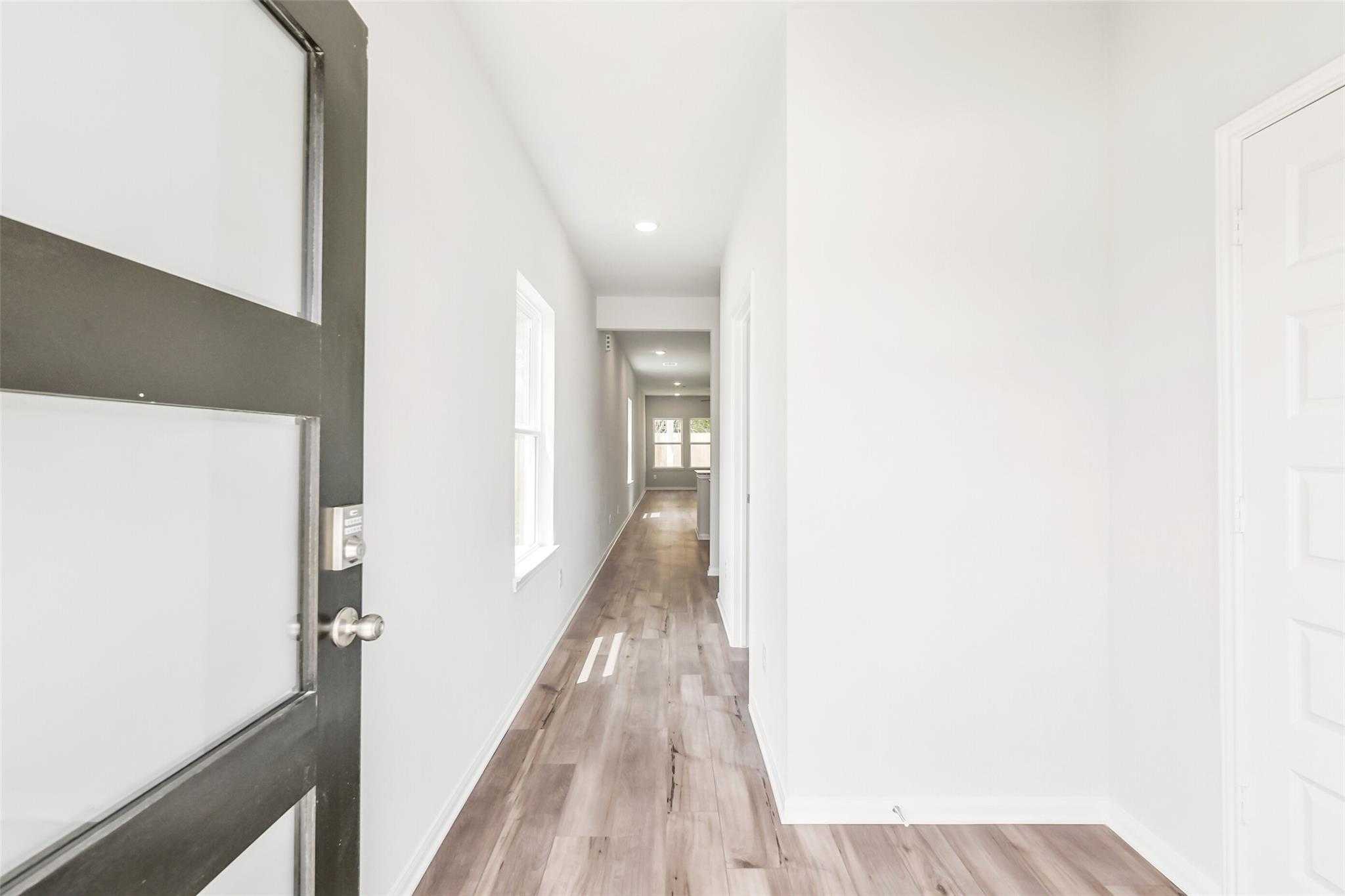 Bright hallway with light wood floors, white walls, and natural light in Davidson Homes The Sabine E, Conroe, Texas