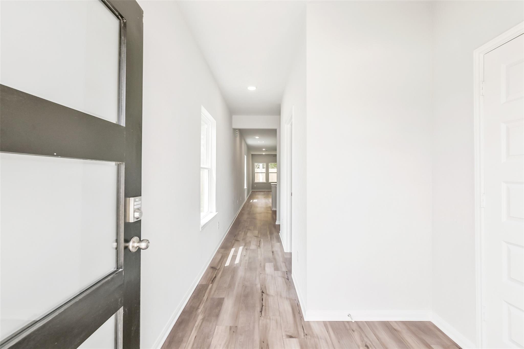 Bright hallway with light wood floors, white walls, and natural light in Davidson Homes The Sabine E, Conroe, Texas