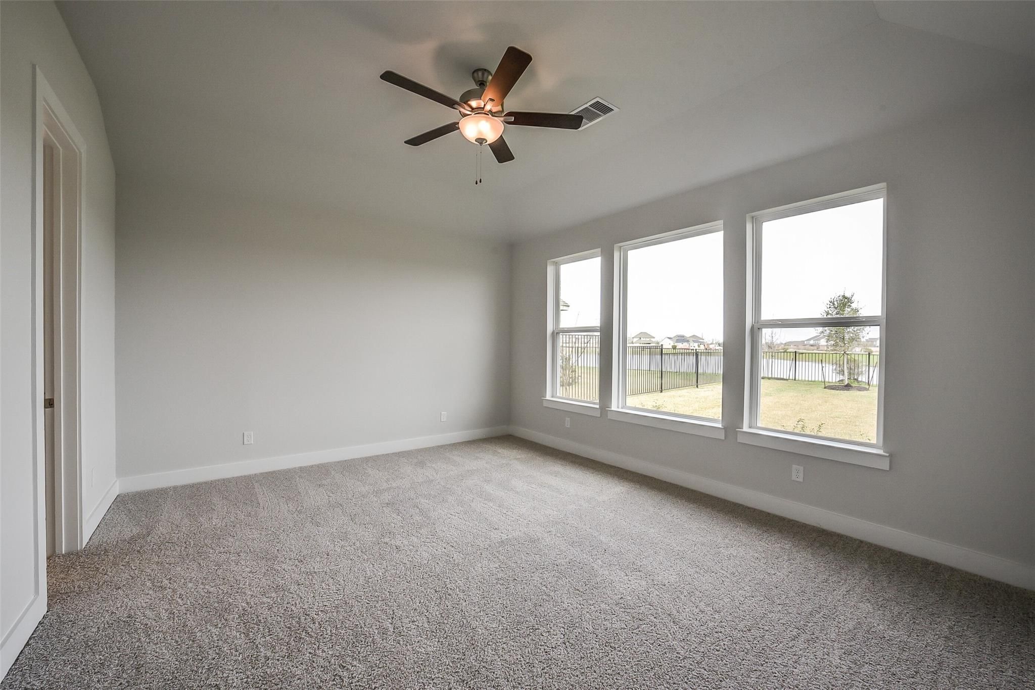Bright bedroom with ceiling fan, carpet flooring, and large windows overlooking fenced backyard in Davidson Homes The Philip B, Rosharon, Texas