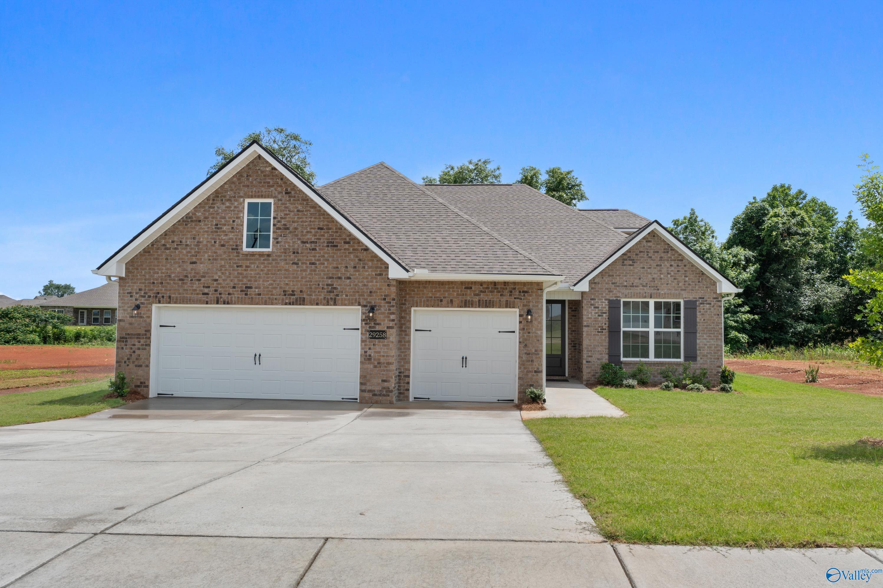Single-story brick home with 3-car garage, white shutters, and manicured lawn in Creekside, Harvest, Alabama