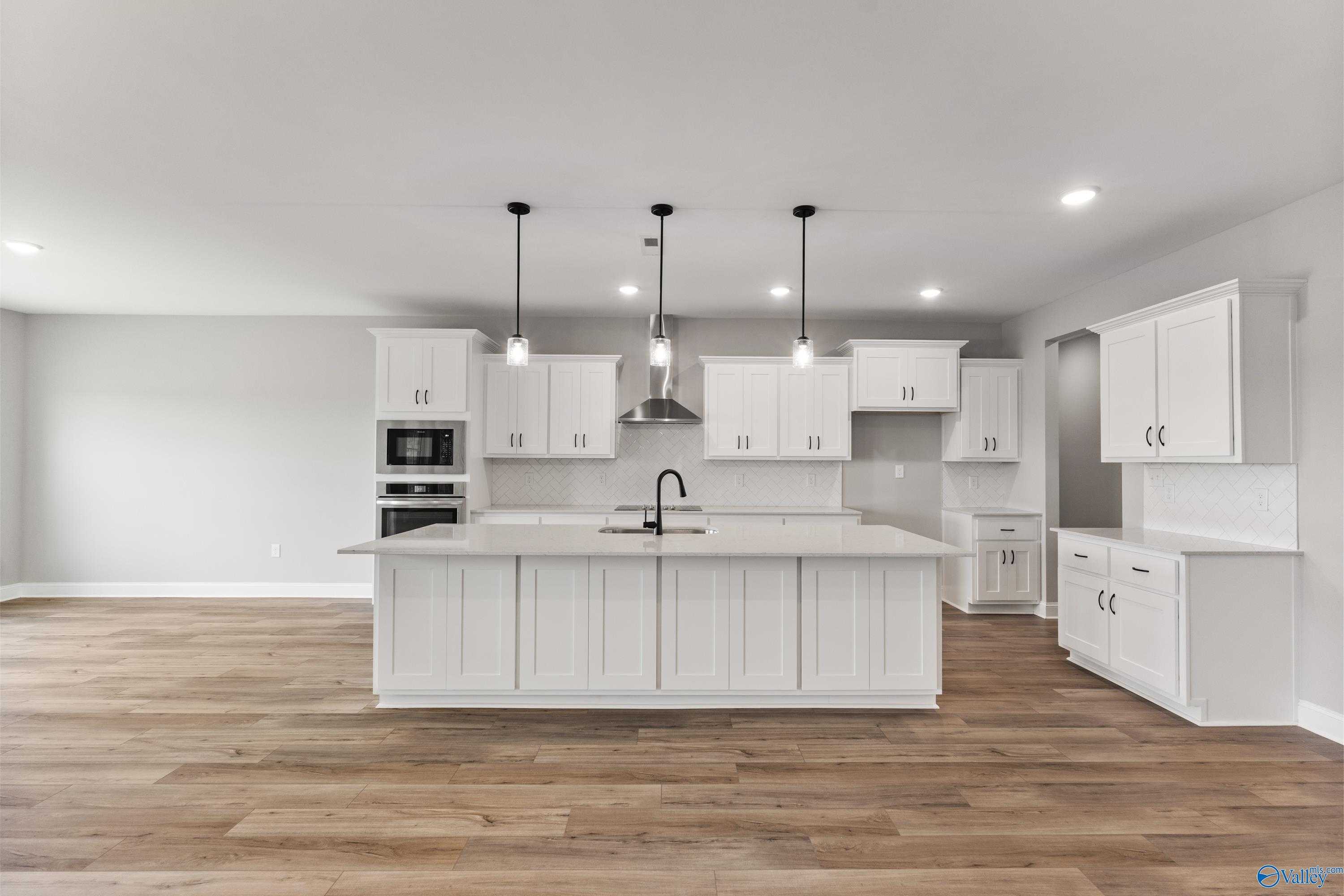 Modern white kitchen with large center island, pendant lights, stainless appliances in Davidson Homes The Finleigh, Toney, AL