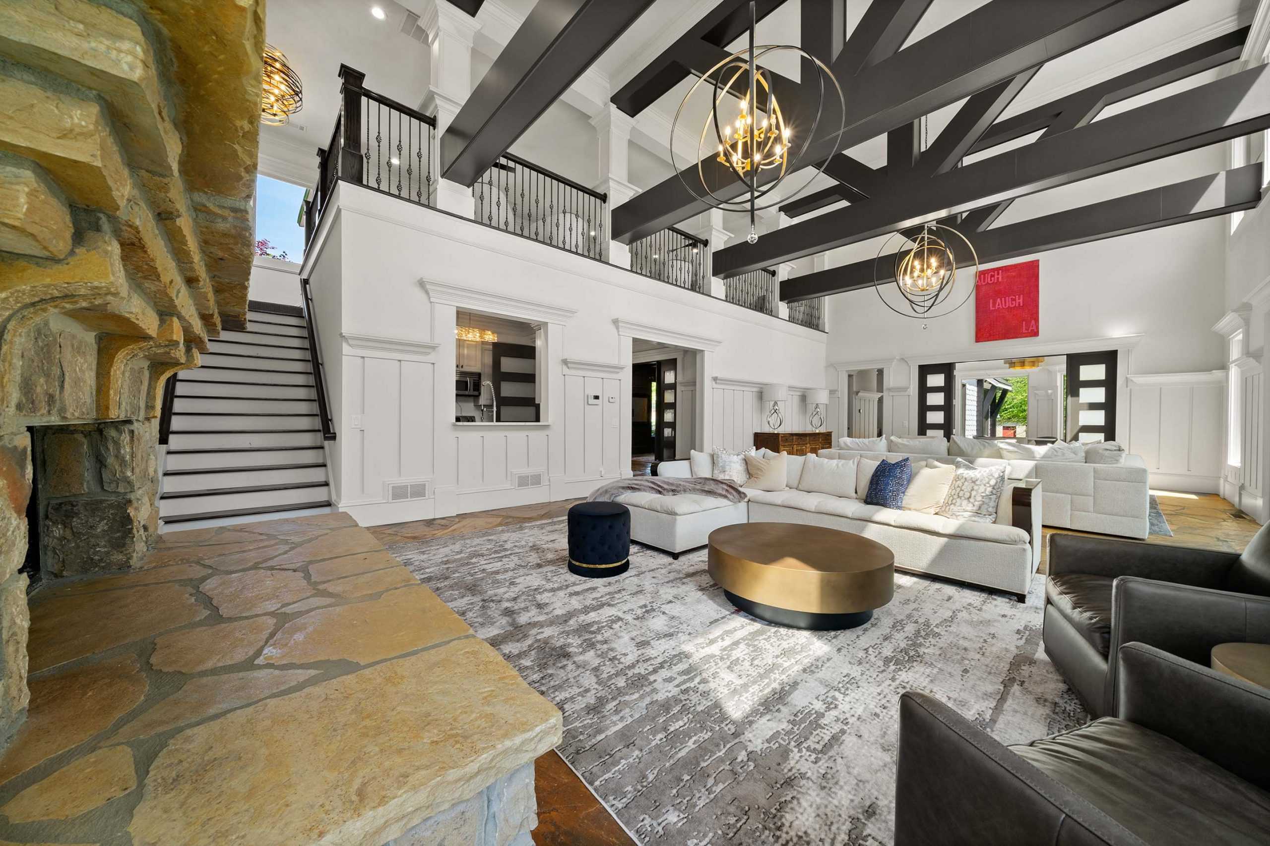 Spacious open-concept great room at Mountainbrook in Cartersville GA with stone fireplace, beamed ceilings, chandeliers, and modern white sofas