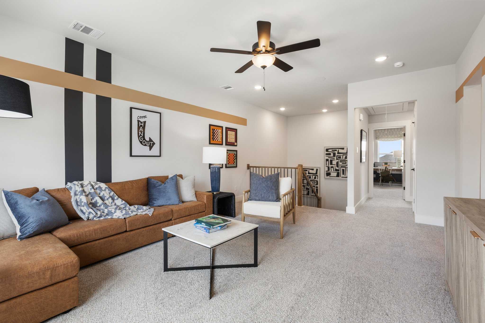 Cozy upstairs loft in The Sequoia home design with tan leather sectional, blue pillows, ceiling fan, and hallway access