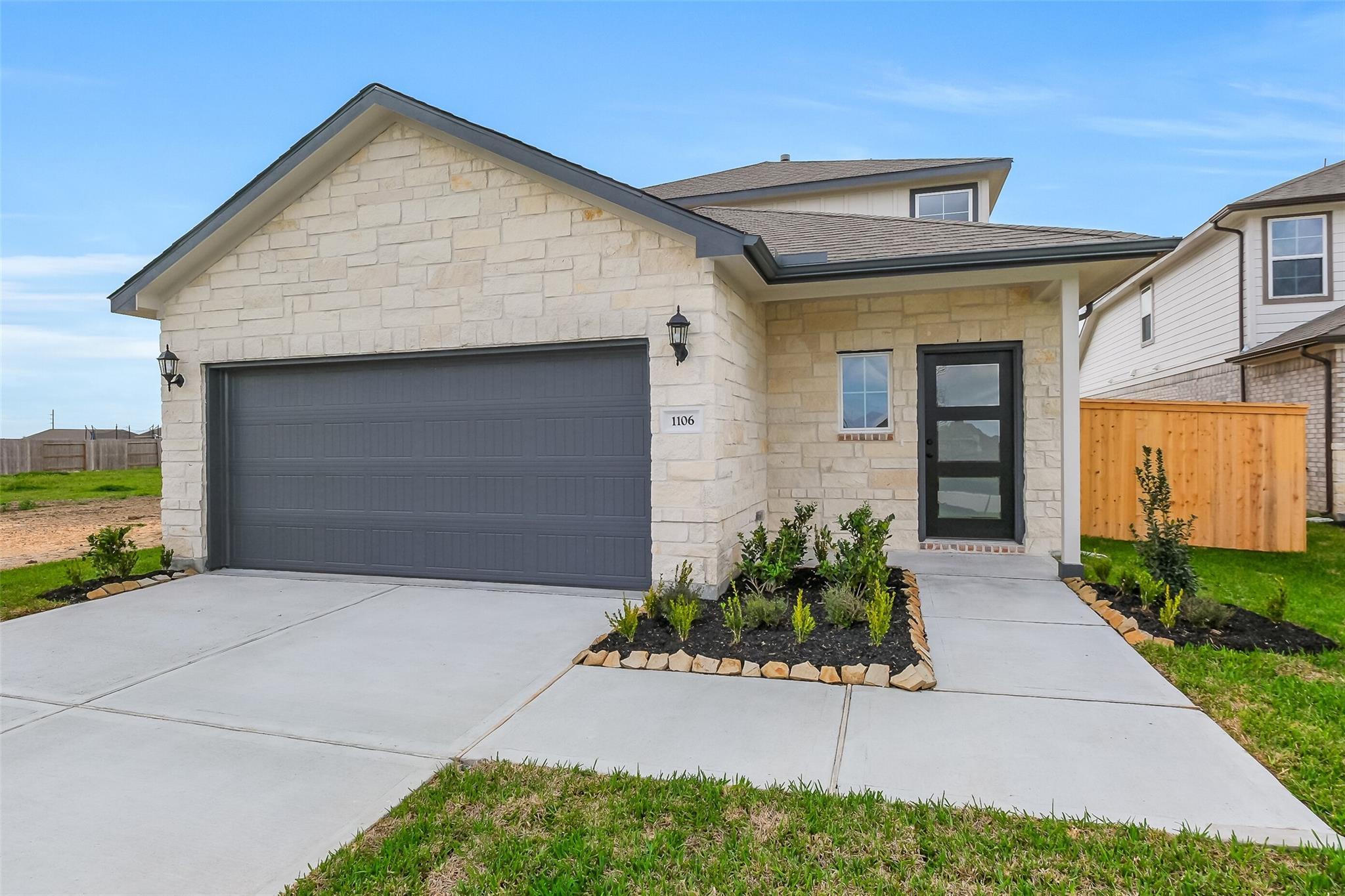 Modern two-story stone home with gray two-car garage, glass front door, and landscaped driveway in Emberly, Beasley, Texas
