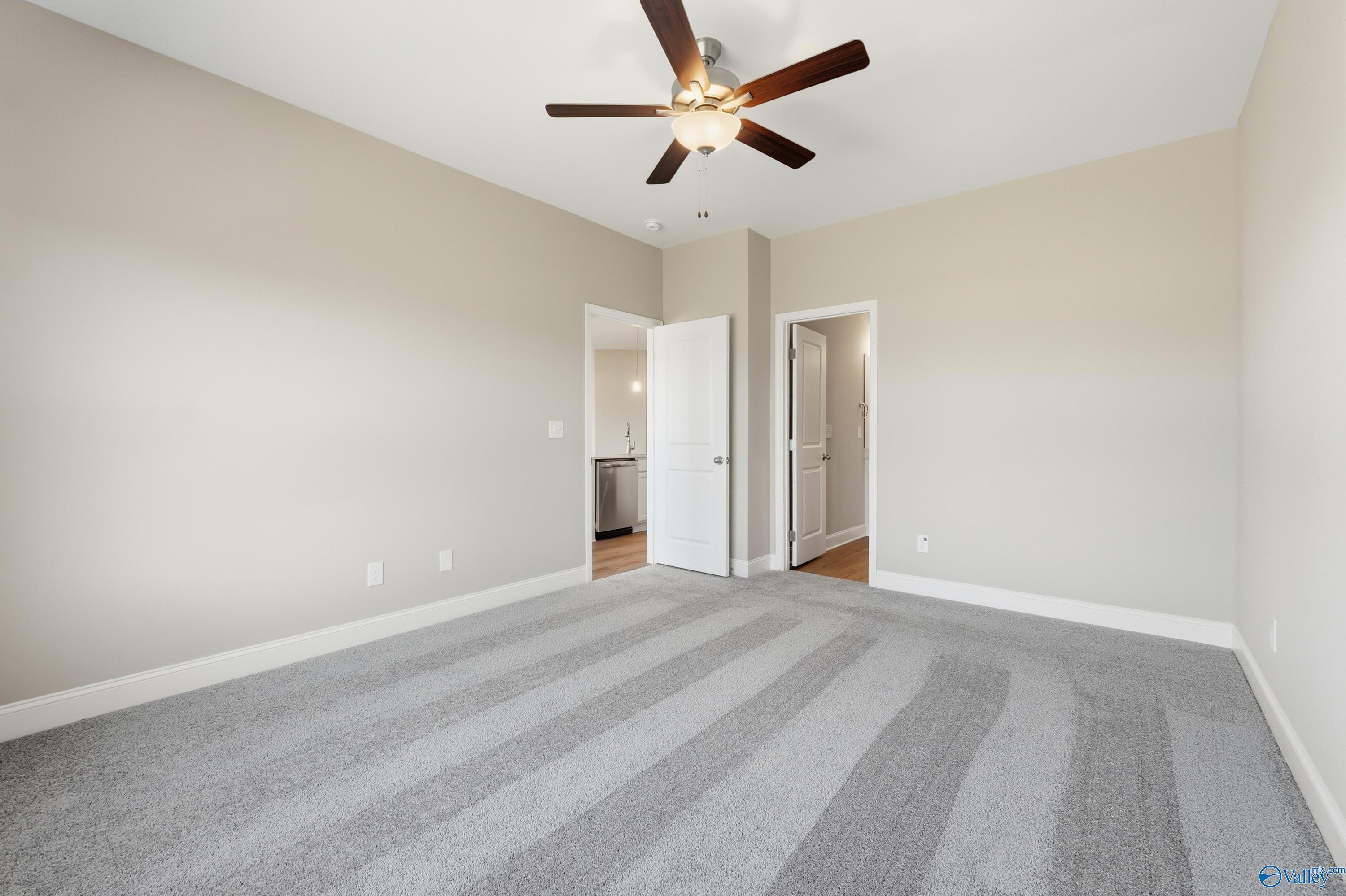 Spacious bedroom with beige walls, ceiling fan, and open bathroom door on striped carpet in Davidson Homes The Franklin C, New Market, Alabama