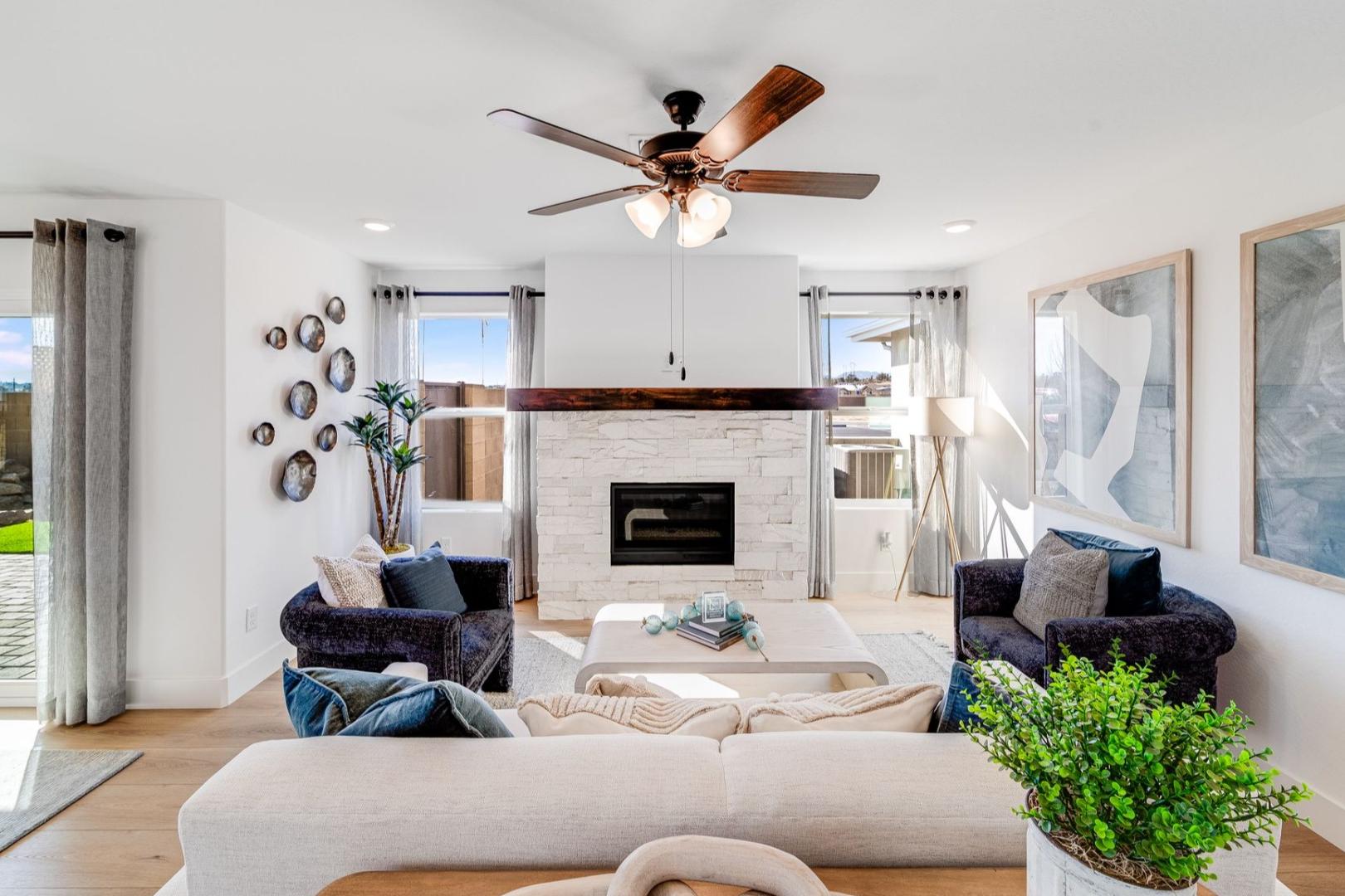 Spacious living room in The Wilmington with beige sectional sofa, stone fireplace, ceiling fans, and large windows to patio