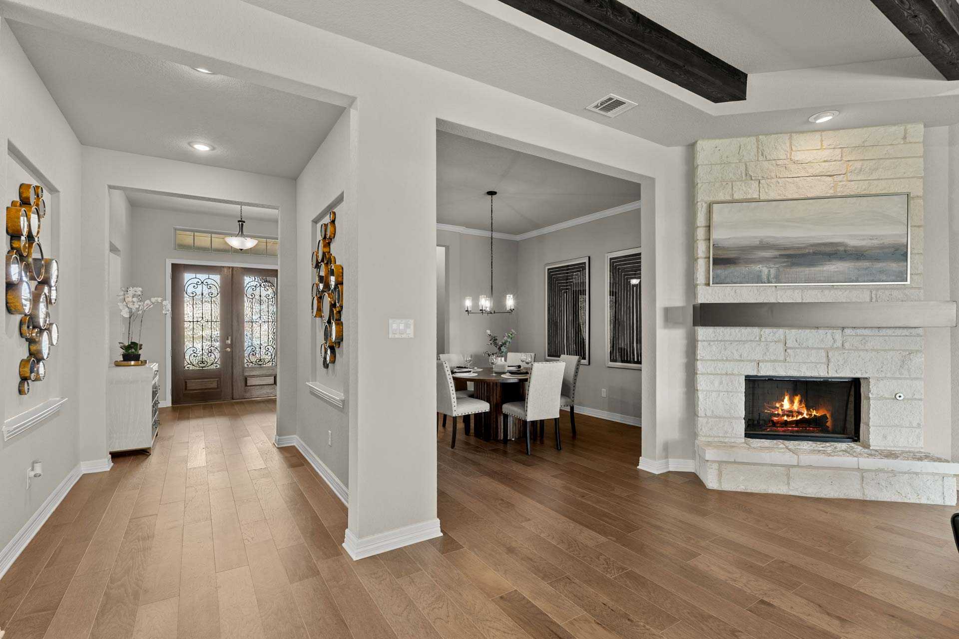 Spacious open-concept hallway and dining area in The Summerlin B home featuring stone fireplace, hardwood floors, Davidson Homes Castroville TX
