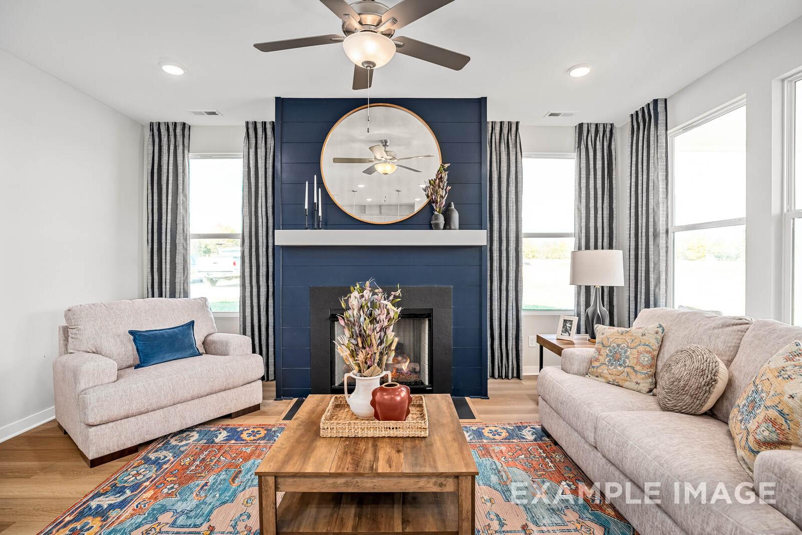 Cozy living room in The Franklin B showcasing navy blue accent wall, round mirror over fireplace, beige sofas, and wooden coffee table