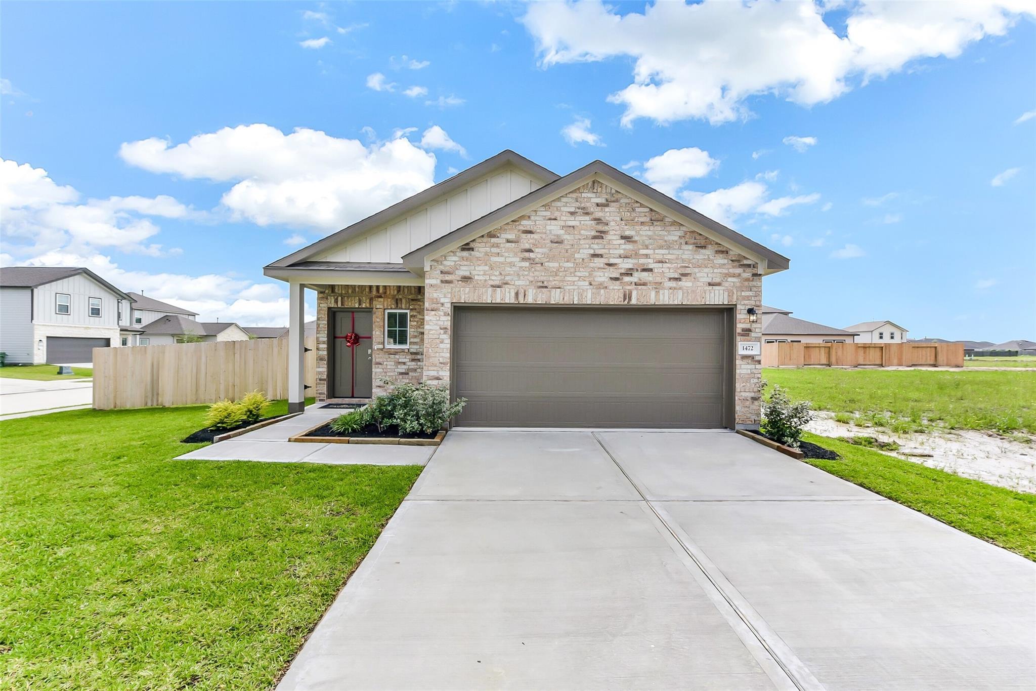 Modern two-story brick home with two-car garage, front porch wreath, and landscaped yard in The Villages at WestPointe, Dayton, Texas