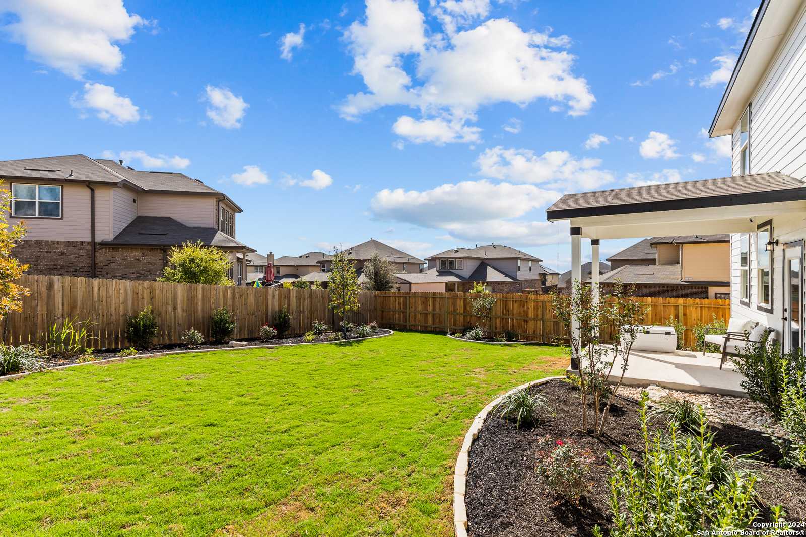 Covered patio with columns overlooking lush green backyard, privacy fence, and landscaping in Davidson Homes The Douglas F, Bricewood, San Antonio