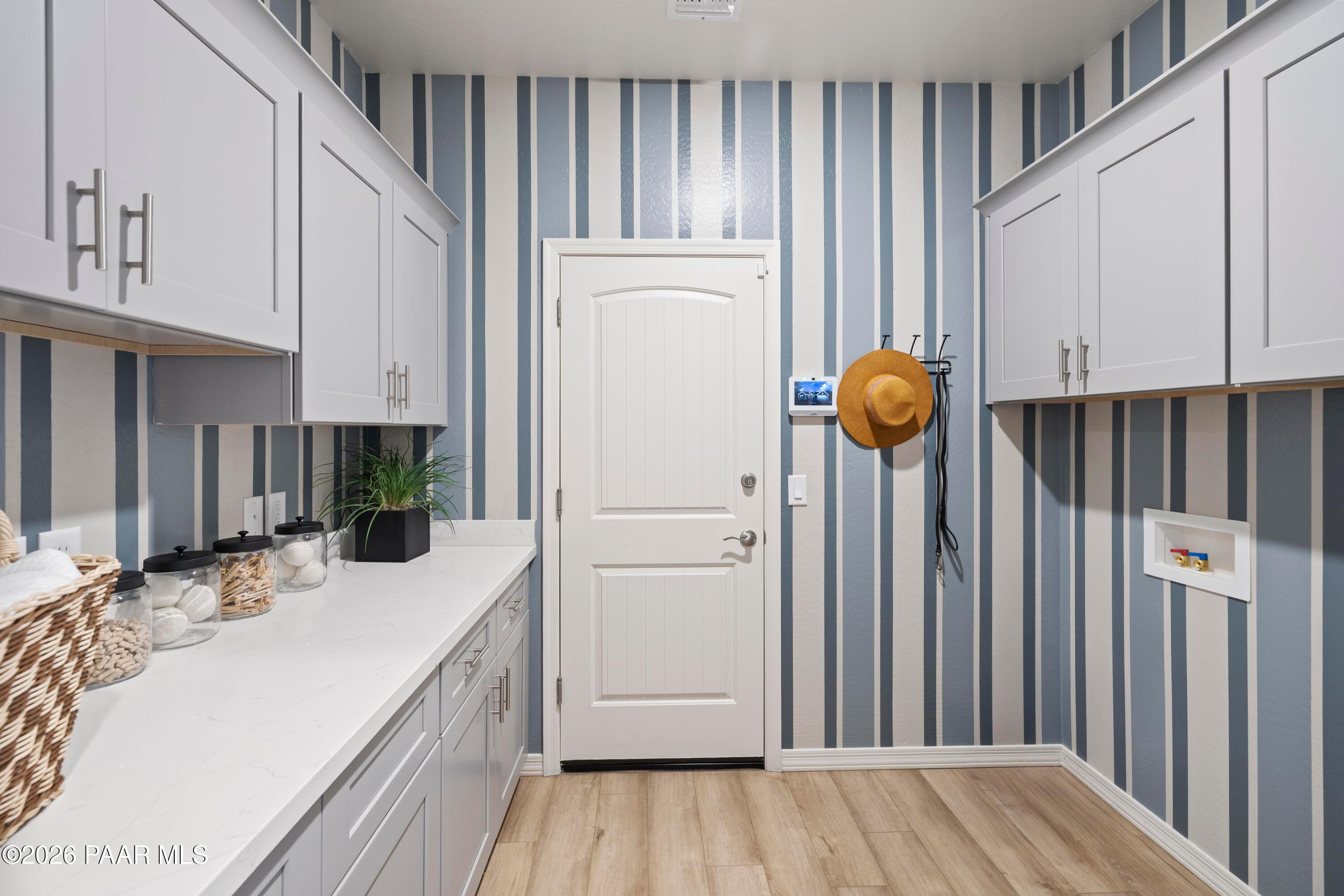 Laundry room with white cabinets, quartz countertops, and blue striped wallpaper in The Harmony A, Pronghorn Ranch.