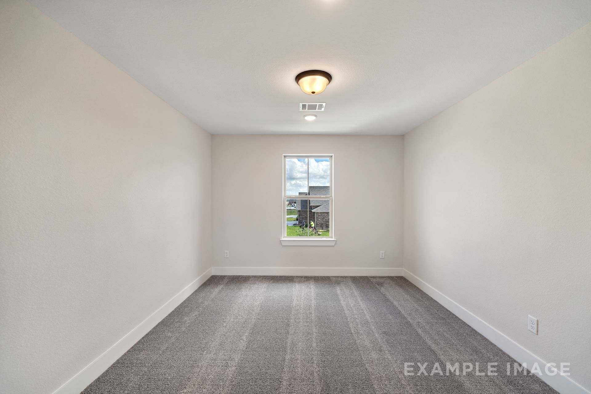 Spacious empty bedroom in The Victoria A home design with beige walls, gray carpet floor, and window overlooking yard