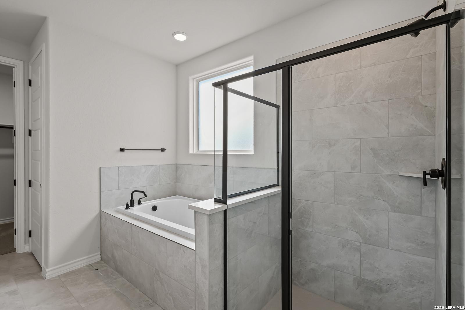 Modern master bathroom with soaking tub, glass walk-in shower, and gray tile in Davidson Homes Oxford F, Castroville, Texas