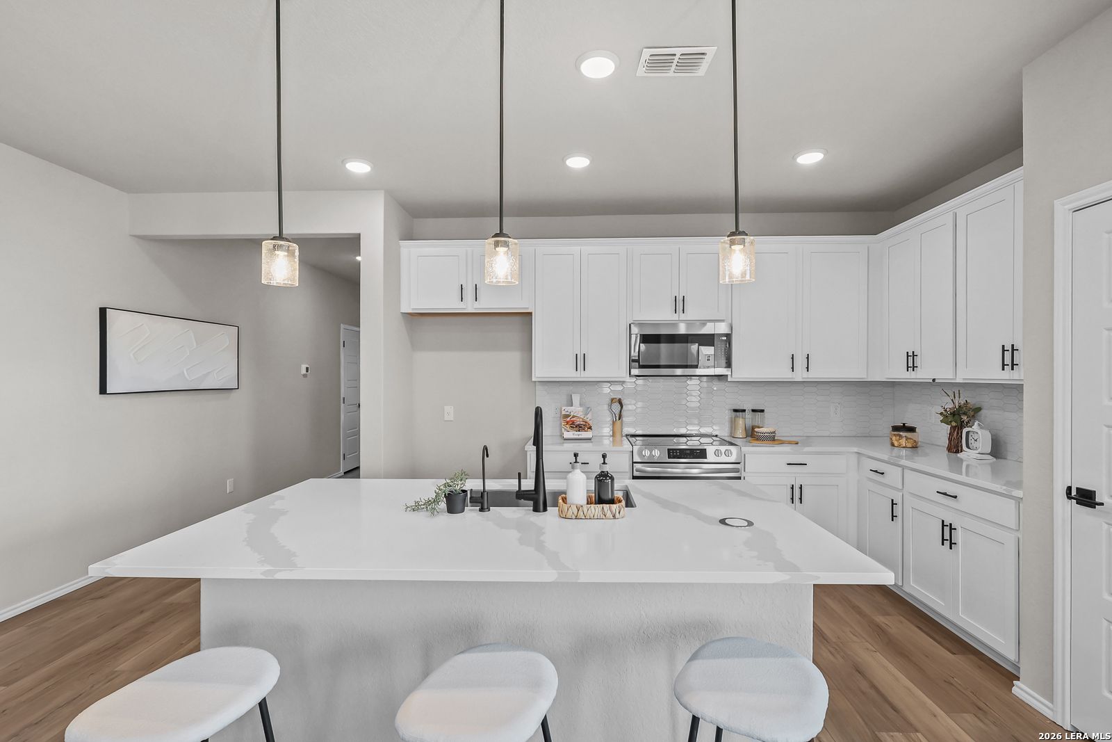 Modern kitchen with white cabinets, quartz island, and pendant lighting in The Daphne H floor plan, Hannah Heights, Seguin.