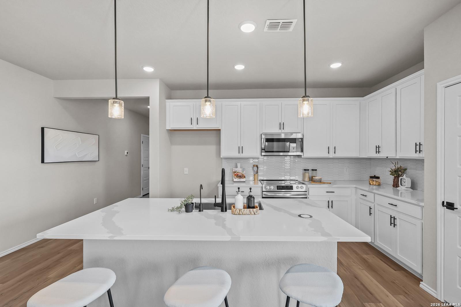 Modern kitchen with white cabinets, quartz island, and pendant lighting in The Daphne H floor plan, Hannah Heights, Seguin.