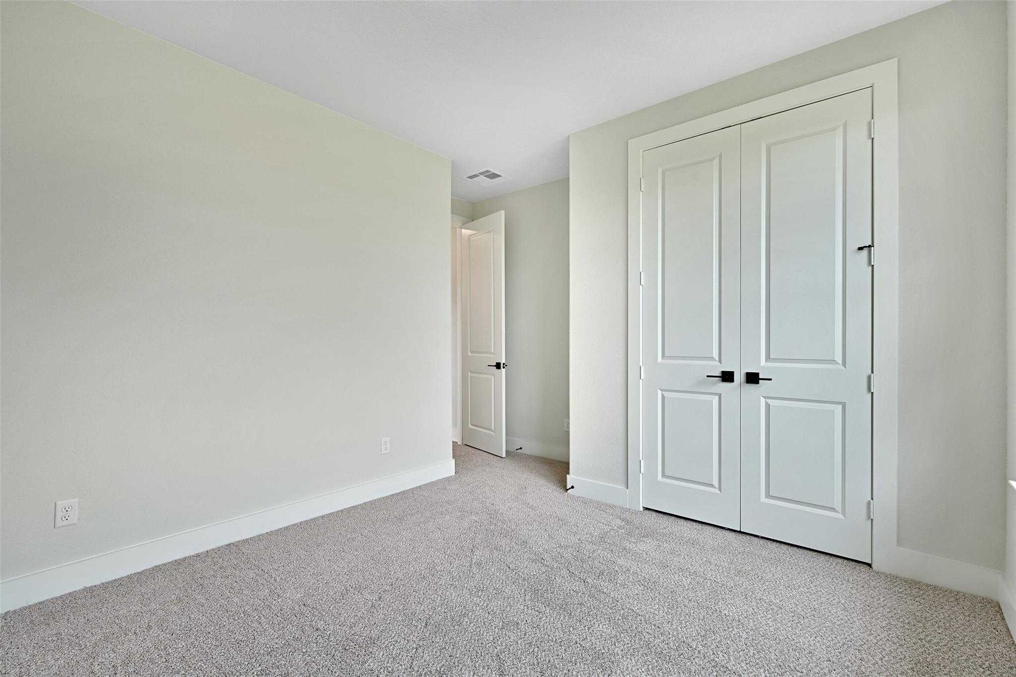 Spacious secondary bedroom with light green walls, beige carpet, and walk-in closet in Davidson Homes The Edward C, Lago Mar, Texas