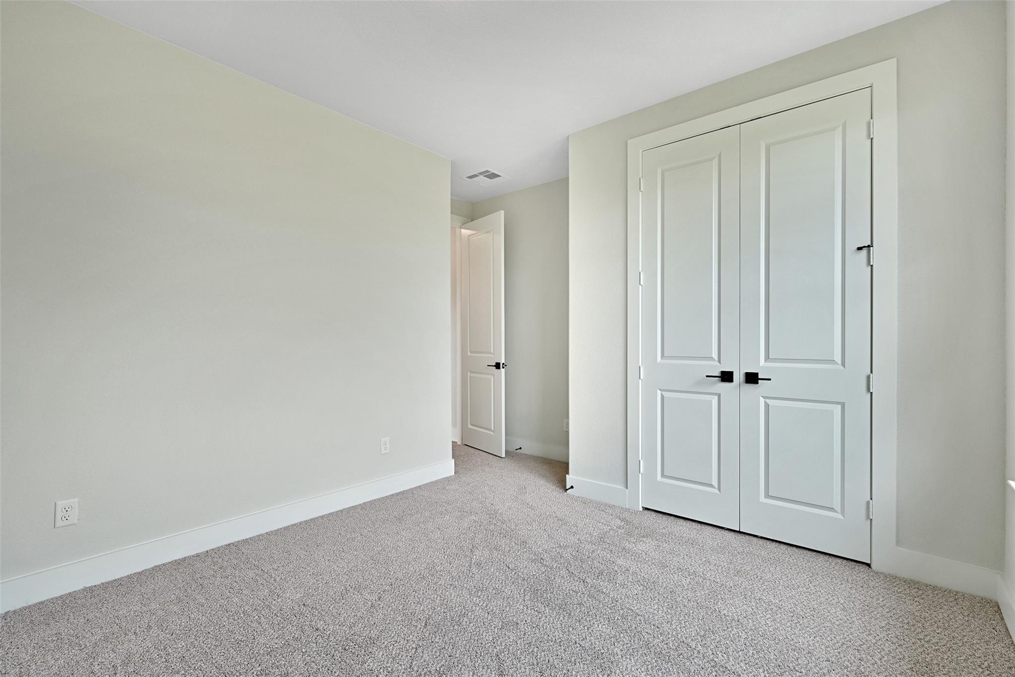 Spacious secondary bedroom with light green walls, beige carpet, and walk-in closet in Davidson Homes The Edward C, Lago Mar, Texas