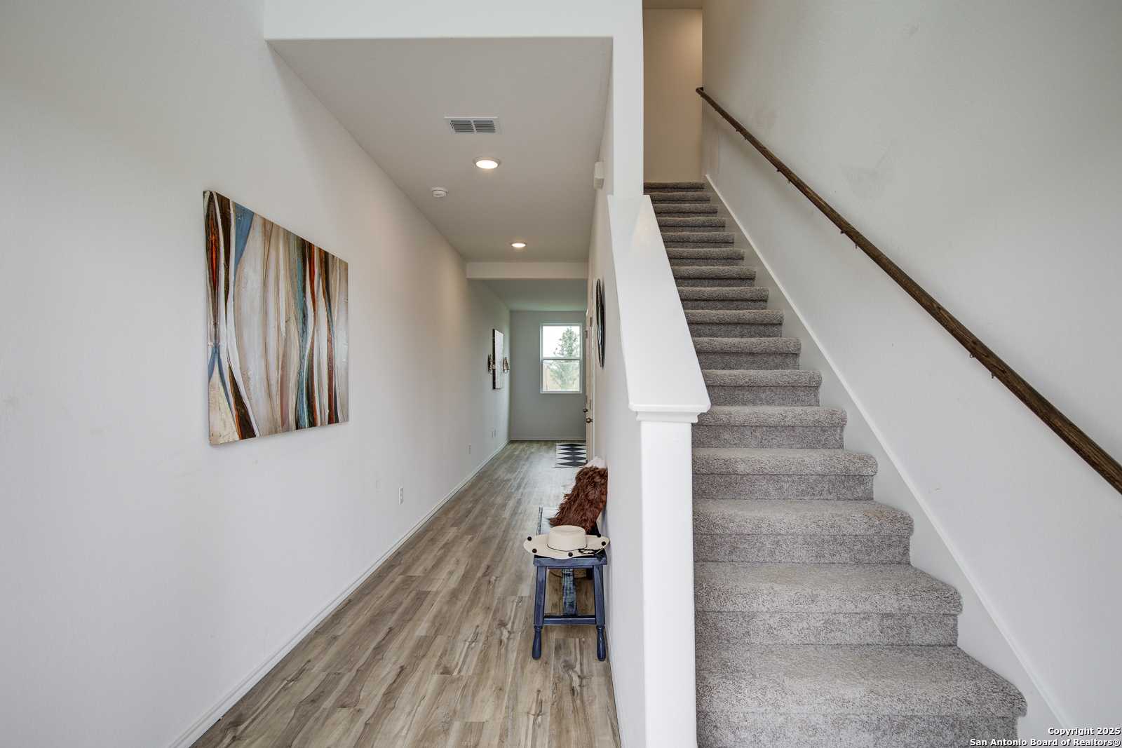 Elegant hallway with carpeted staircase, abstract wall art, wooden bench in Davidson Homes The Trinity A, San Antonio